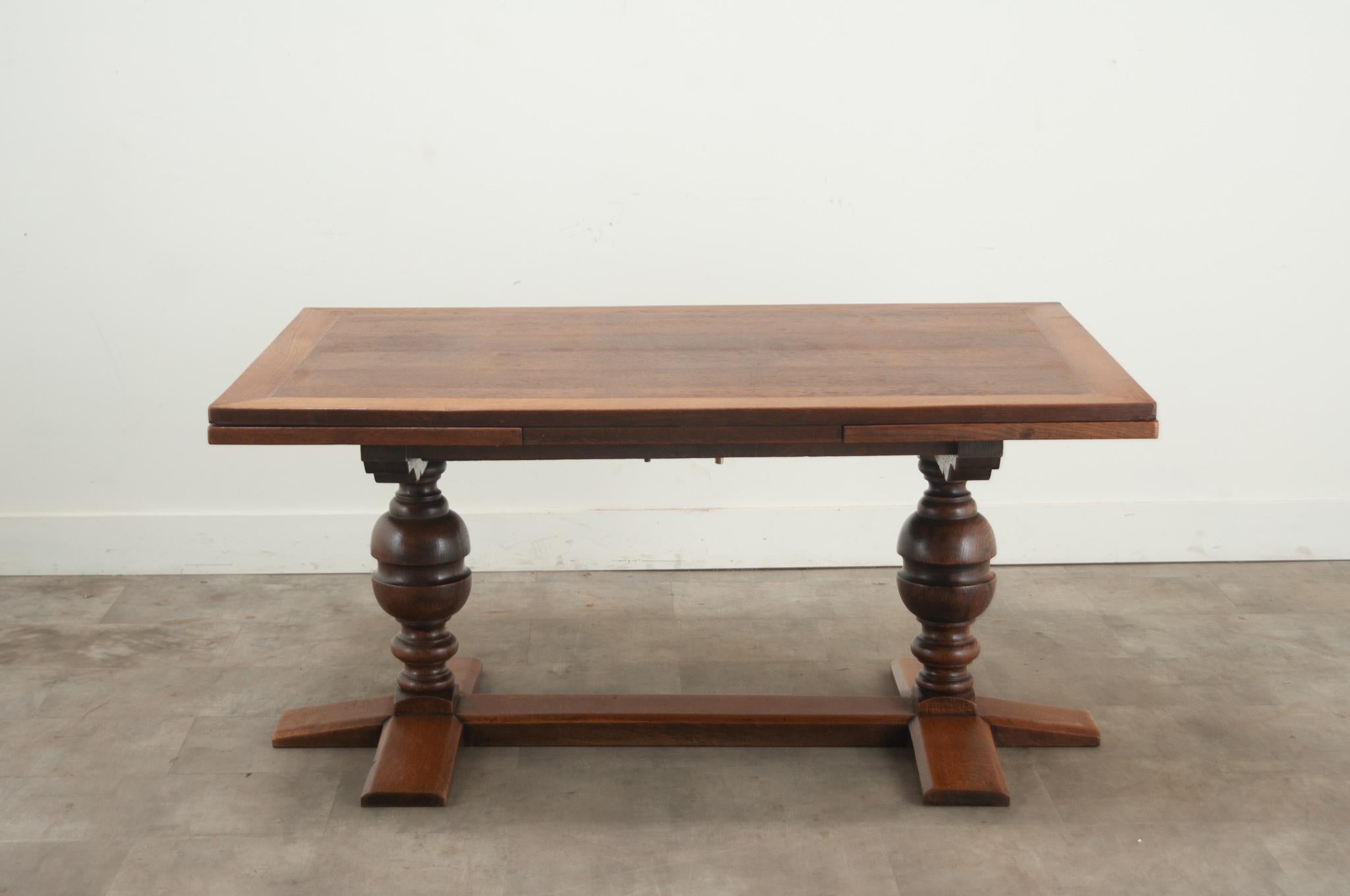 An extending French oak trestle base dining table with two self storing leaves. This versatile table top rests over a trestle base composed of two turned baluster legs joined by a wide stretcher and base. This table has recently been cleaned and