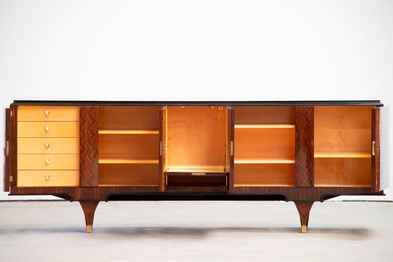 French Art Deco sideboard, credenza, with bar cabinet. The sideboard features stunning Macassar wood grain and rich pattern. It offers ample storage, with shelves, drinks cabinet and a column of drawers. The case rests on tall tapered legs. A unique