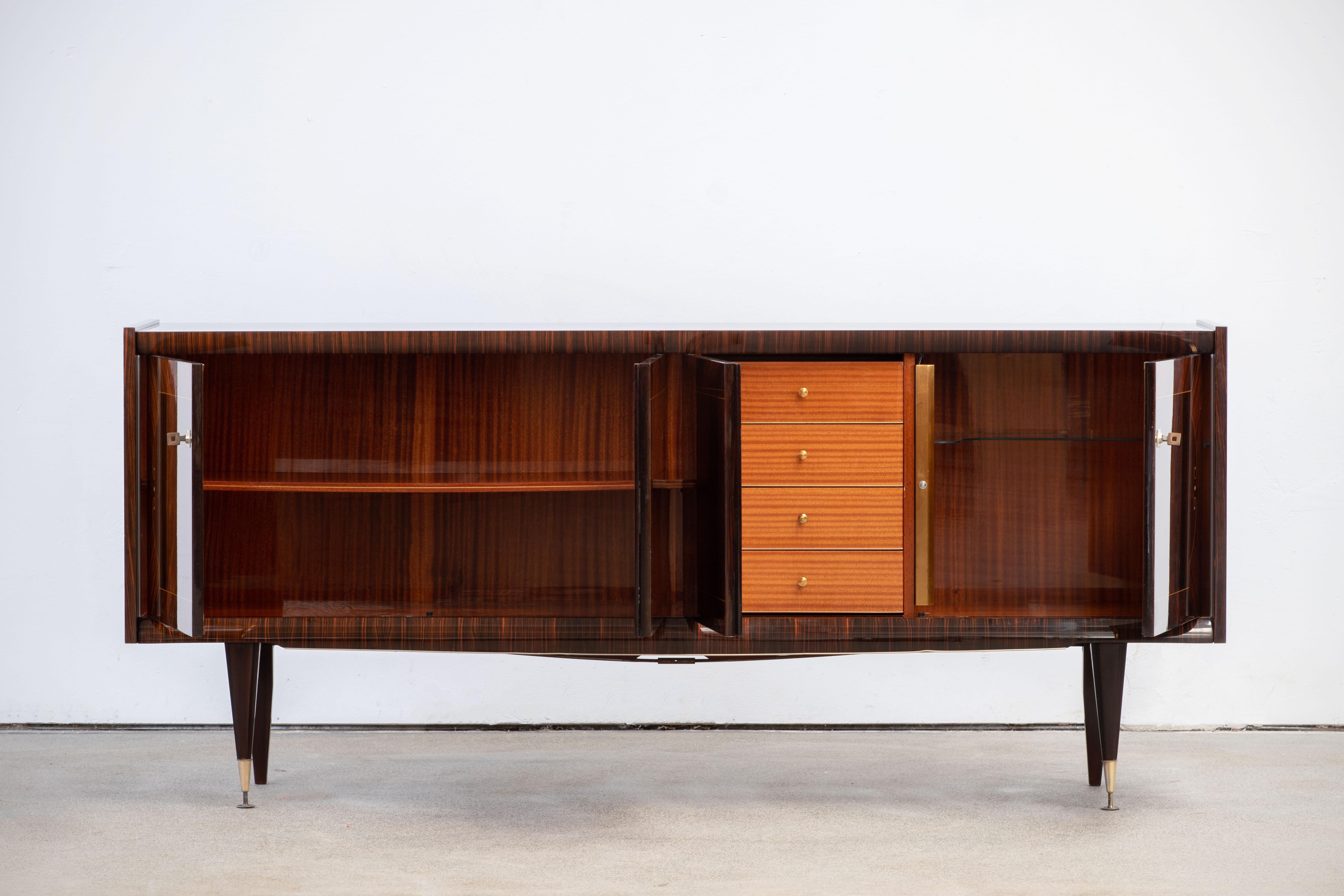 French Art Deco sideboard, credenza, with bar cabinet. The sideboard features stunning Macassar wood grain and rich pattern. It offers ample storage, with shelves and a column of drawers. The case rests on tall tapered legs. A unique blend of Art