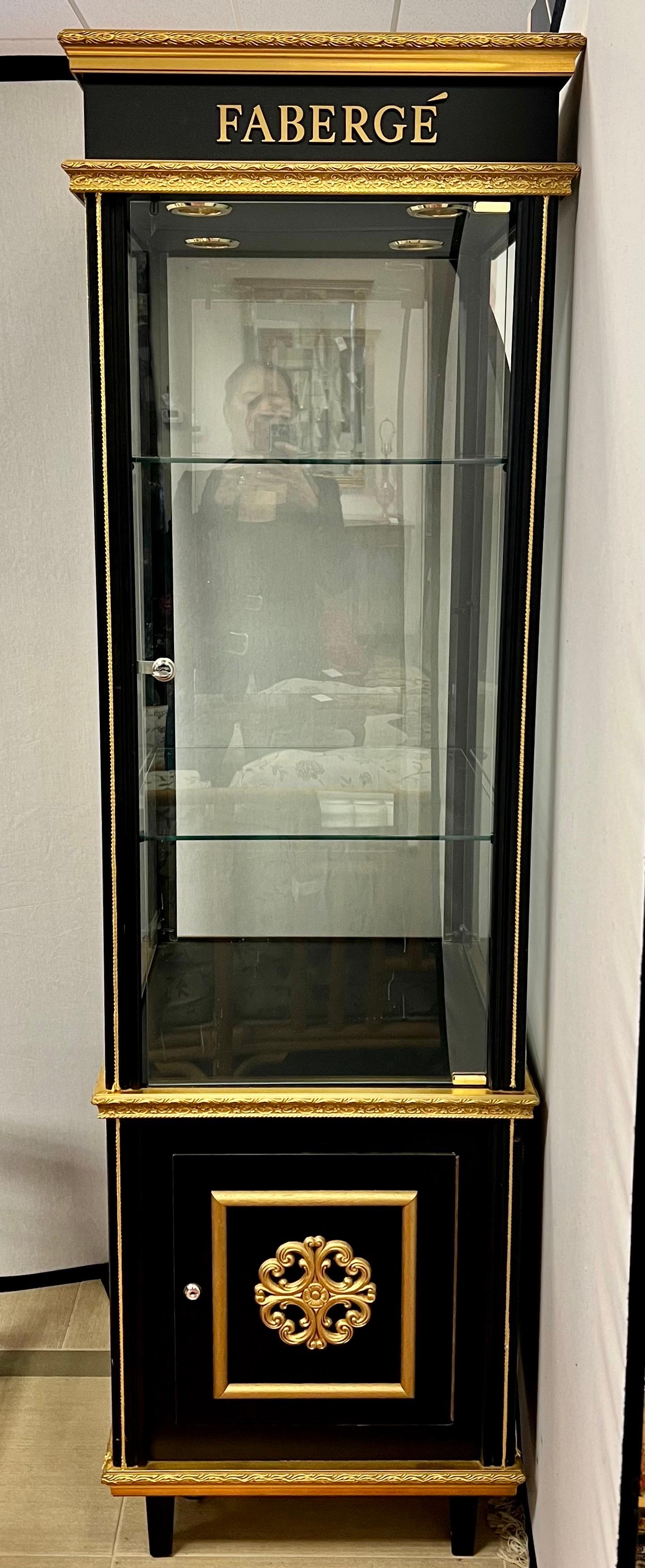 Elegant tall black and gold Faberge display cabinet with four glass panel sides including door with stainless steel lock. Door opens to glass shelves that are illuminated from above. The base has single cabinet door that opens to storage.
Store