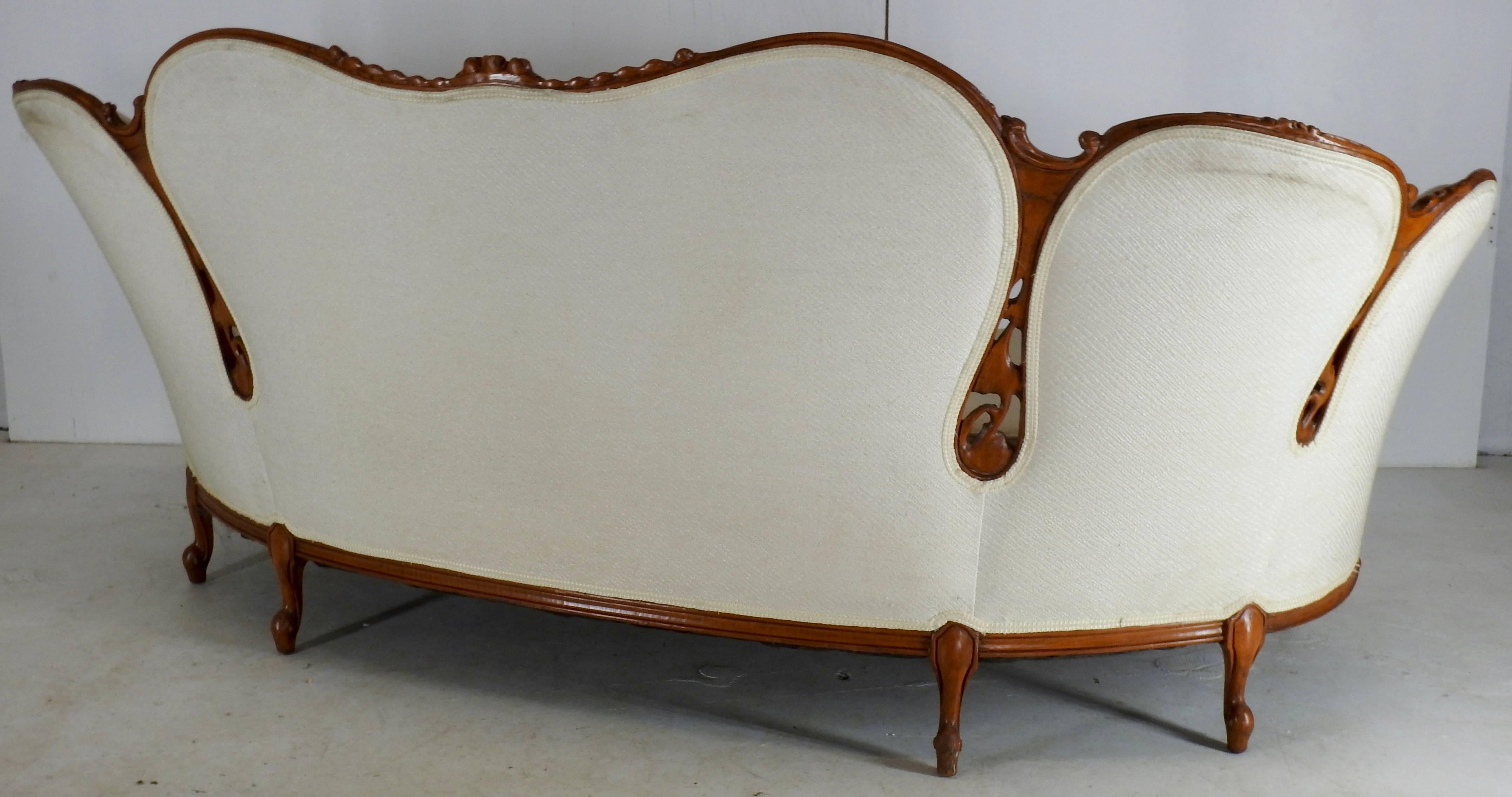Elegance makes up this sofa from the Victorian era. Woven cream color fabric with trim adorns the sofa which has detailed carved wood trim. Graceful curves make up the back and sides which sit atop a snail foot. Cutouts in the wood add to the beauty