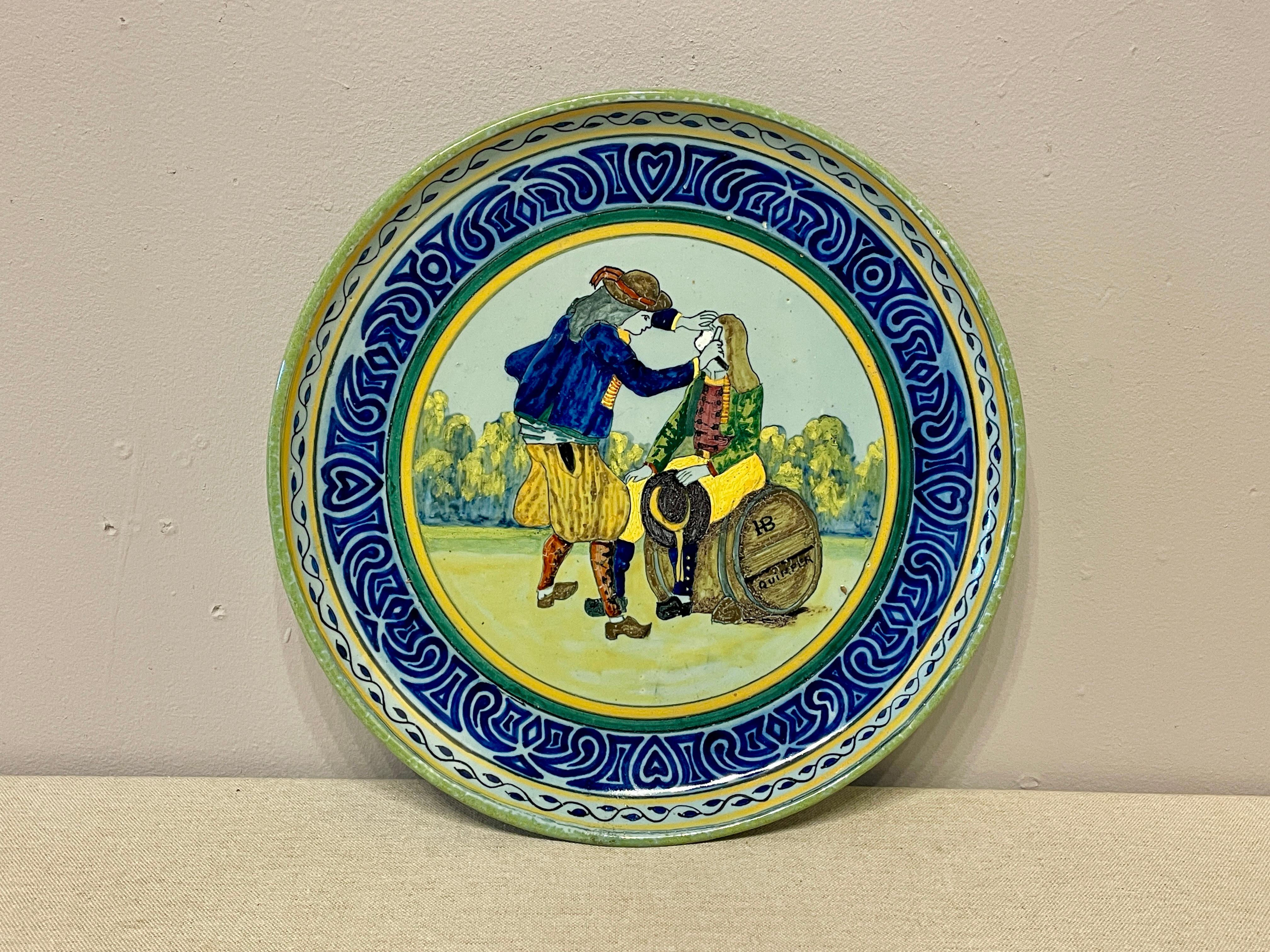 A French large faience platter signed HB Quimper with a blue border, depicting a man shaving another man sitting on a barrel. In great condition with no restorations. Beautiful glazing. circa 1910. 
Dimensions are 12