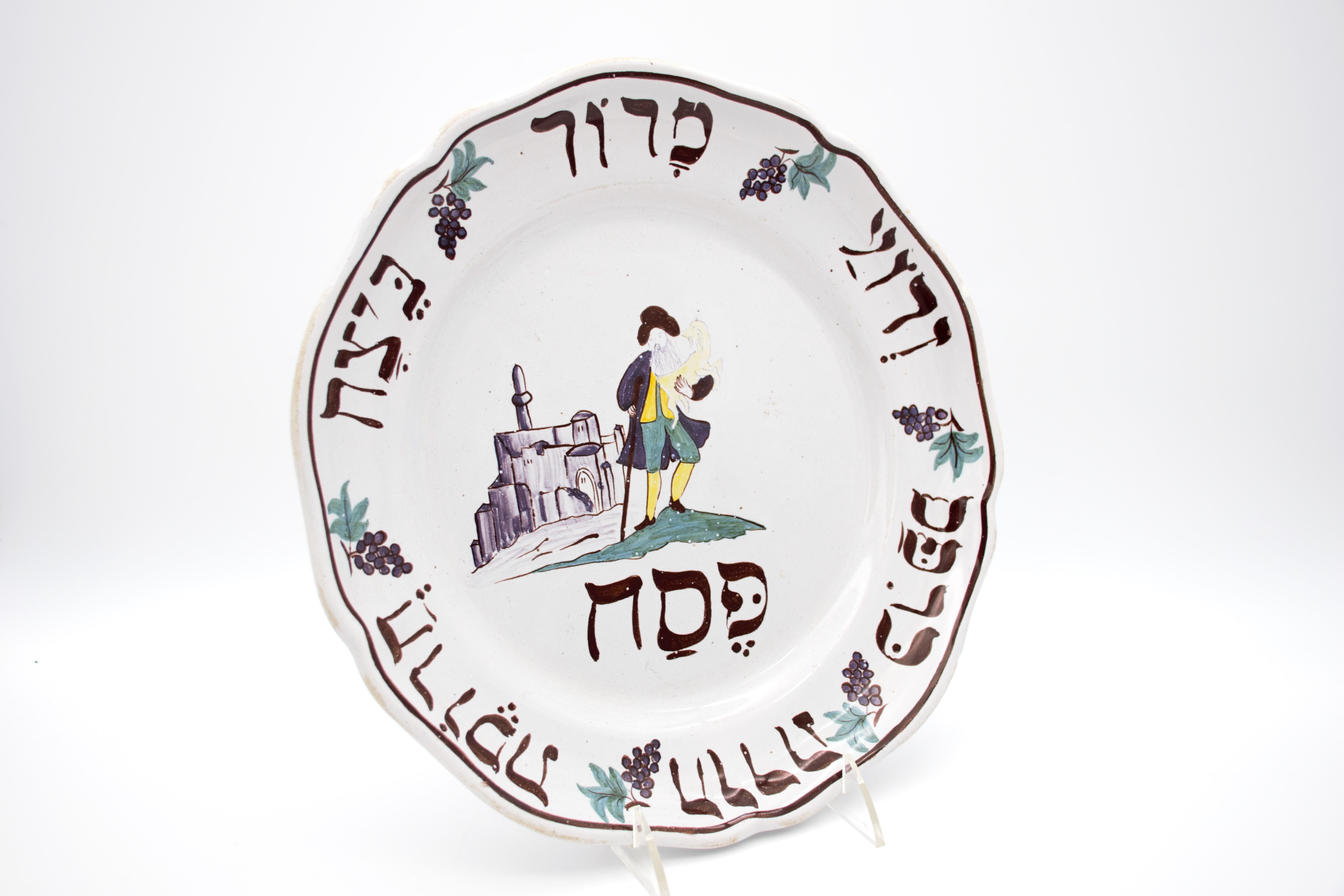 this plate has a creme white background, the center painted with a man holding a lamb before a cityscape, probably a depiction of Jerusalem by someone who never actually visited the city or even see it, under the man there is the word Passover 