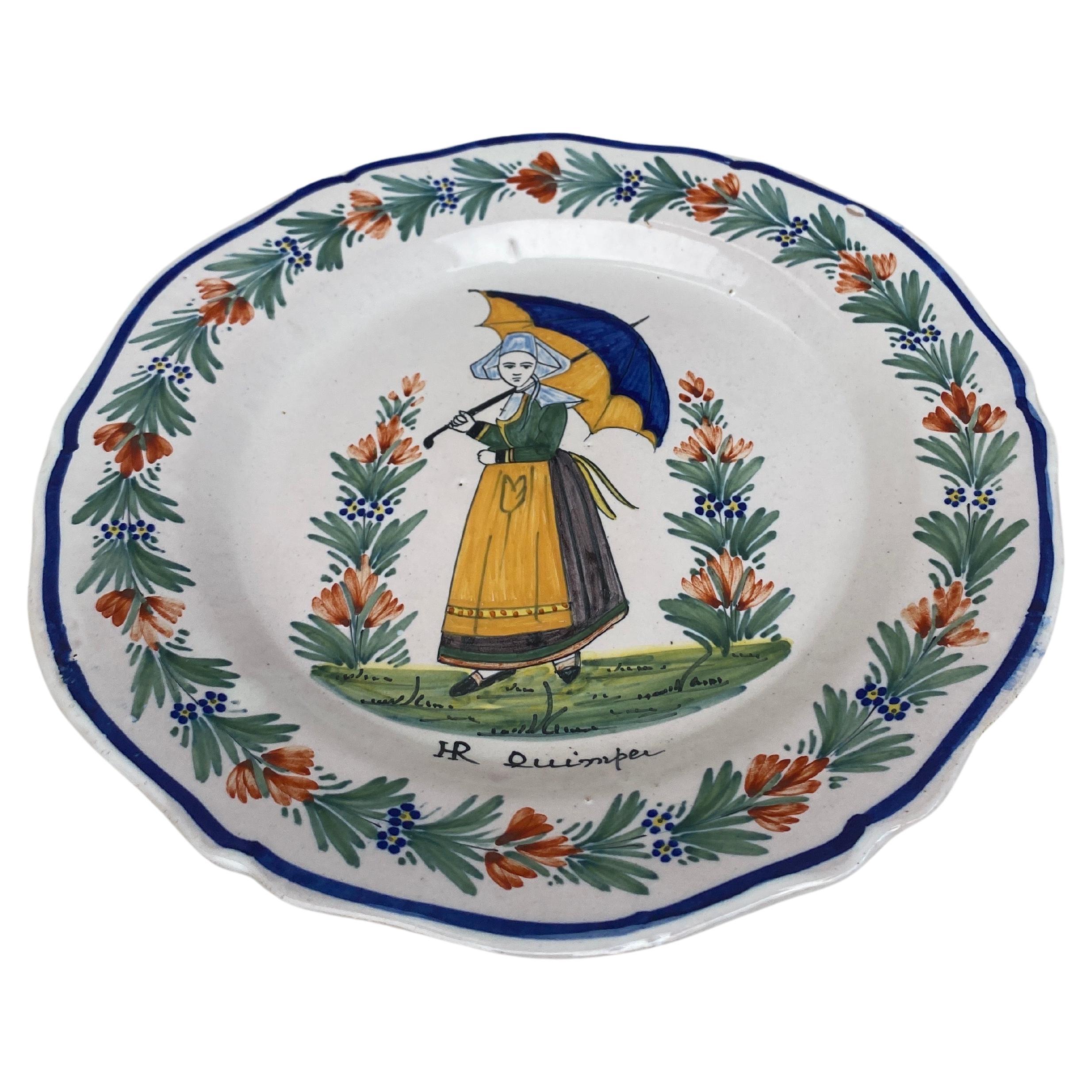 A French faience plate with a farmer with an umbrella signed HR Quimper, circa 1890
border of flowers.
 
