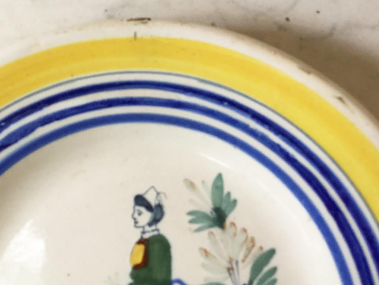 A French faience plate with a bretonne farmer in the costume with flowers signed Henriot Quimper, circa 1930.
Colorful border yellow and blue lines.