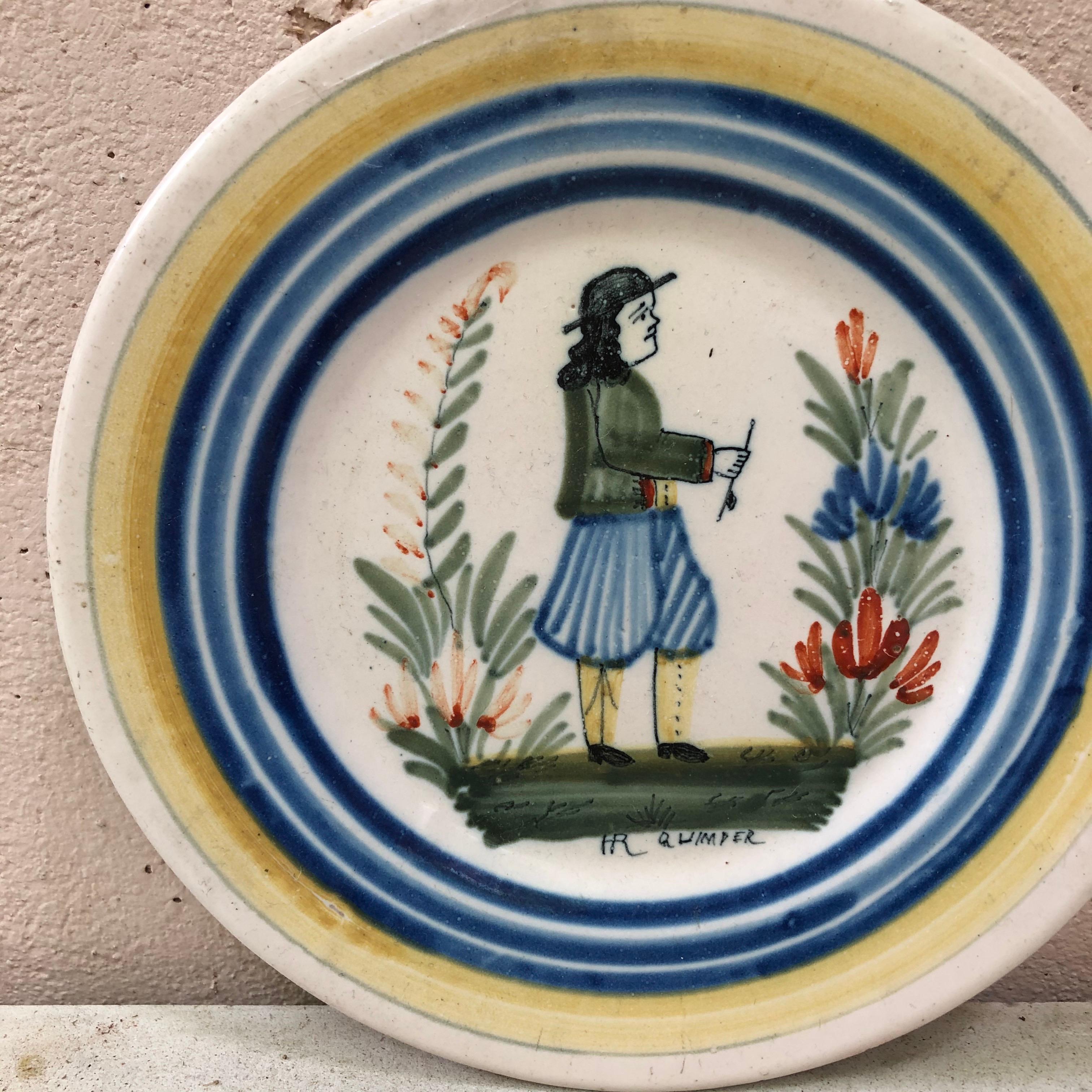 A French faience plate with a Breton farmer in the costume with flowers signed Henriot Quimper, circa 1930.
Colorful yellow border and blue lines.