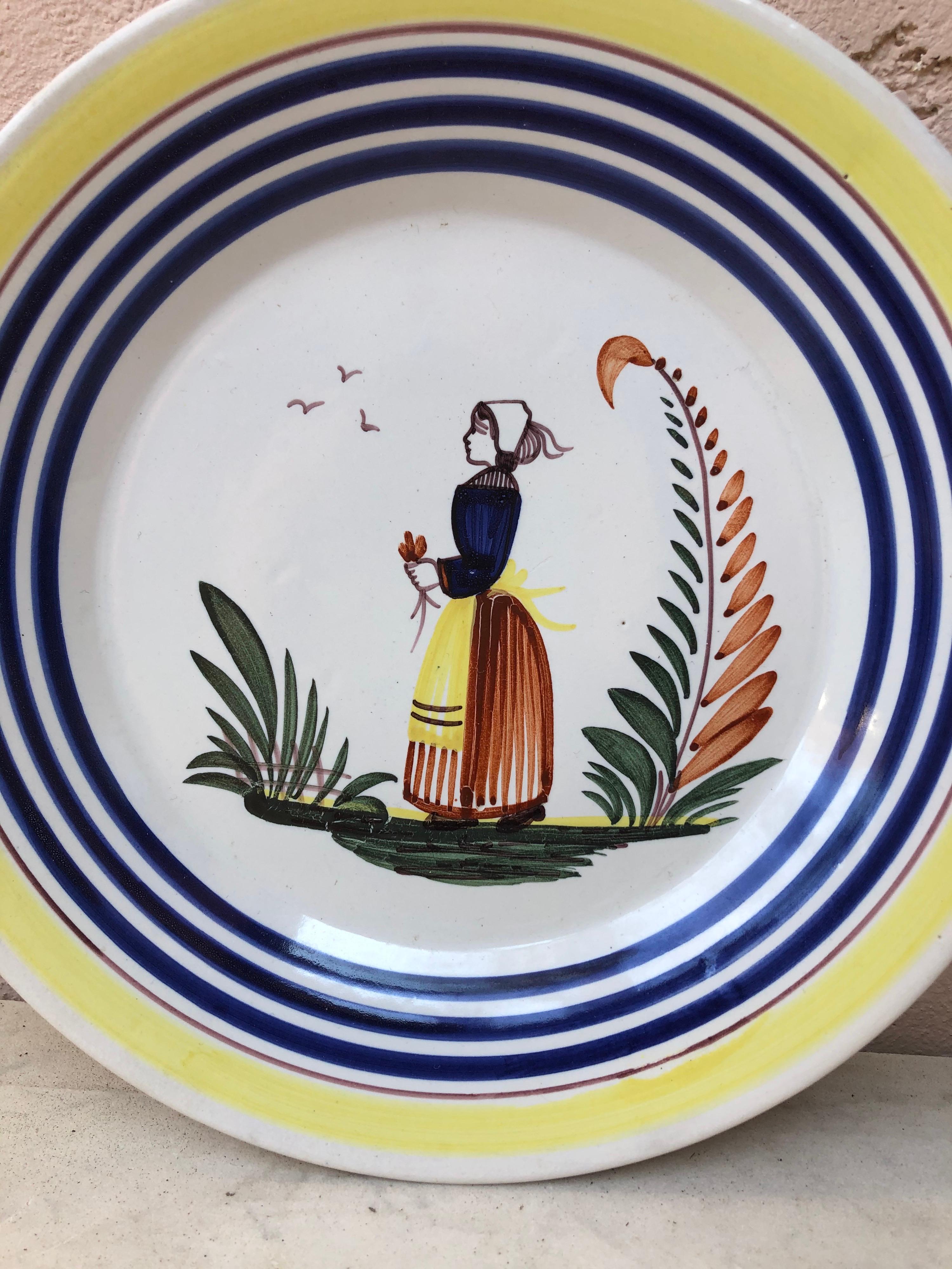 Une grande assiette en faïence française avec un fermier en costume avec des fleurs signée Henriot Quimper, vers 1950.
Bordure jaune colorée et lignes bleues.
Mesure : 9,5 de diamètre.