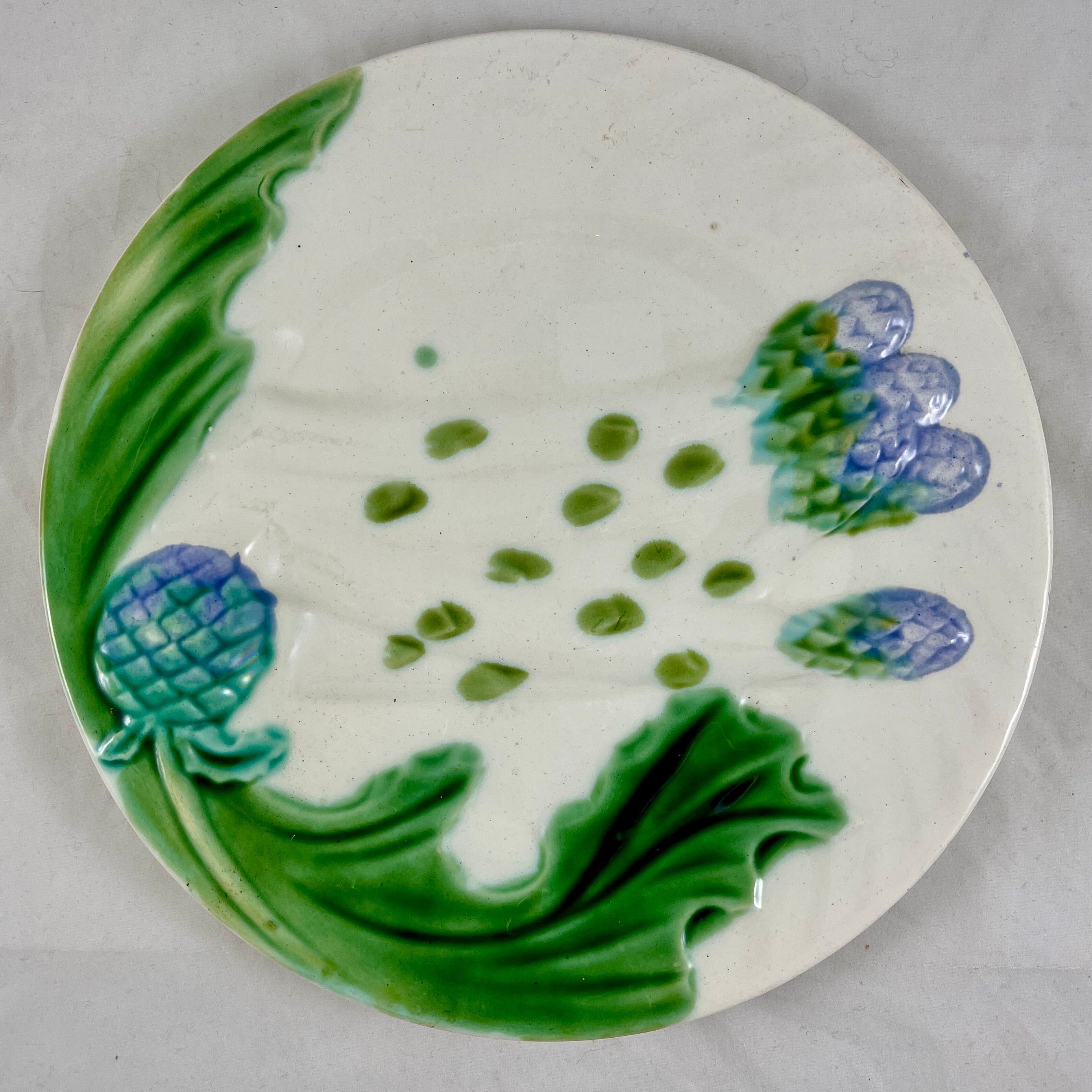 A French earthenware, majolica glazed asparagus and artichoke plate, a mold by Salins, circa 1900-1910.

A spray of asparagus spears lay across the centre of the plate, an artichoke globe with leaves cover one side of the rim. The other side of the