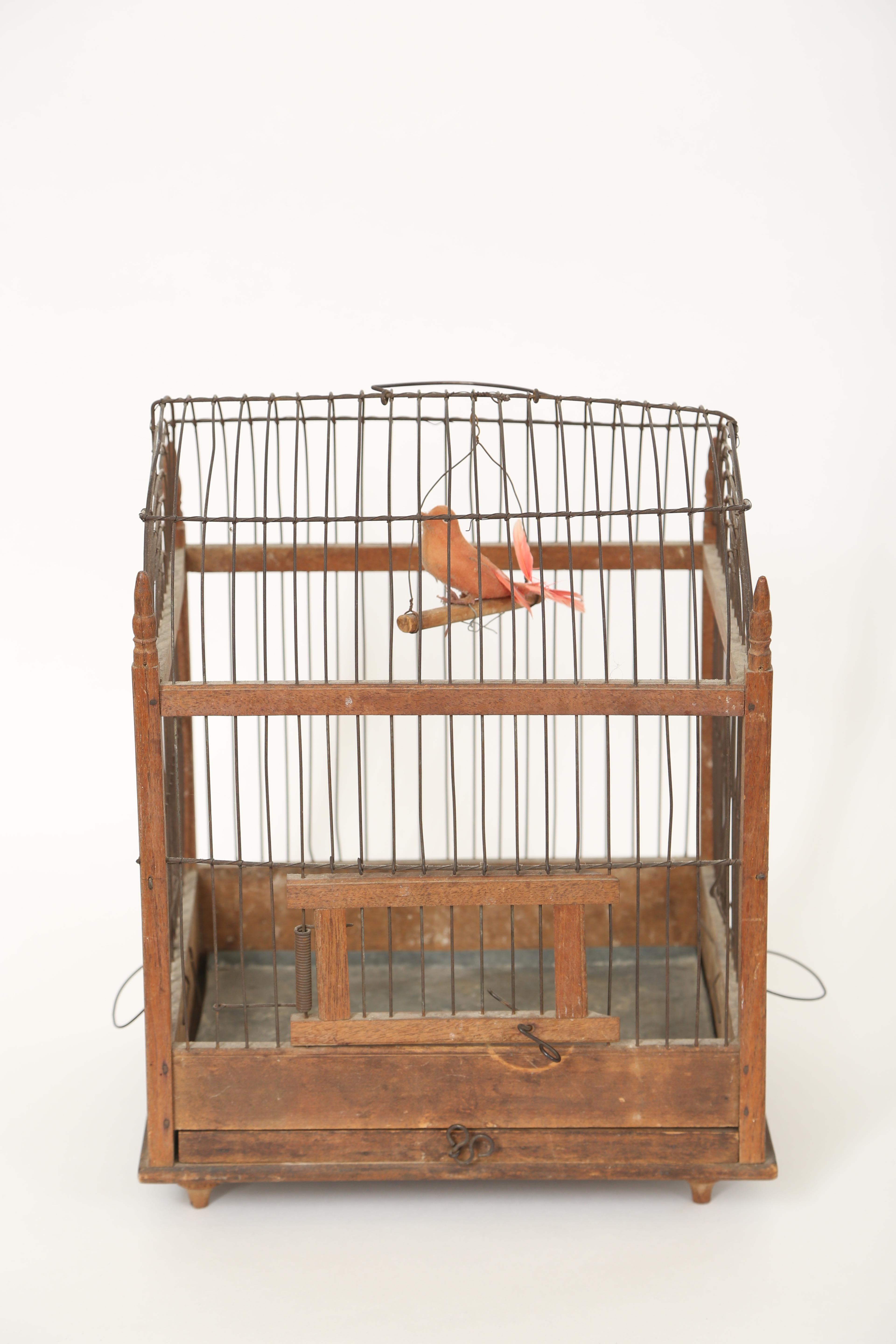 This French country wooden birdcage has charming original appeal. The sides have fan top detail in the wirework. Each corner has a turned finial. The door latches and there is a slide out metal lined tray at the bottom of the cage all of which rests