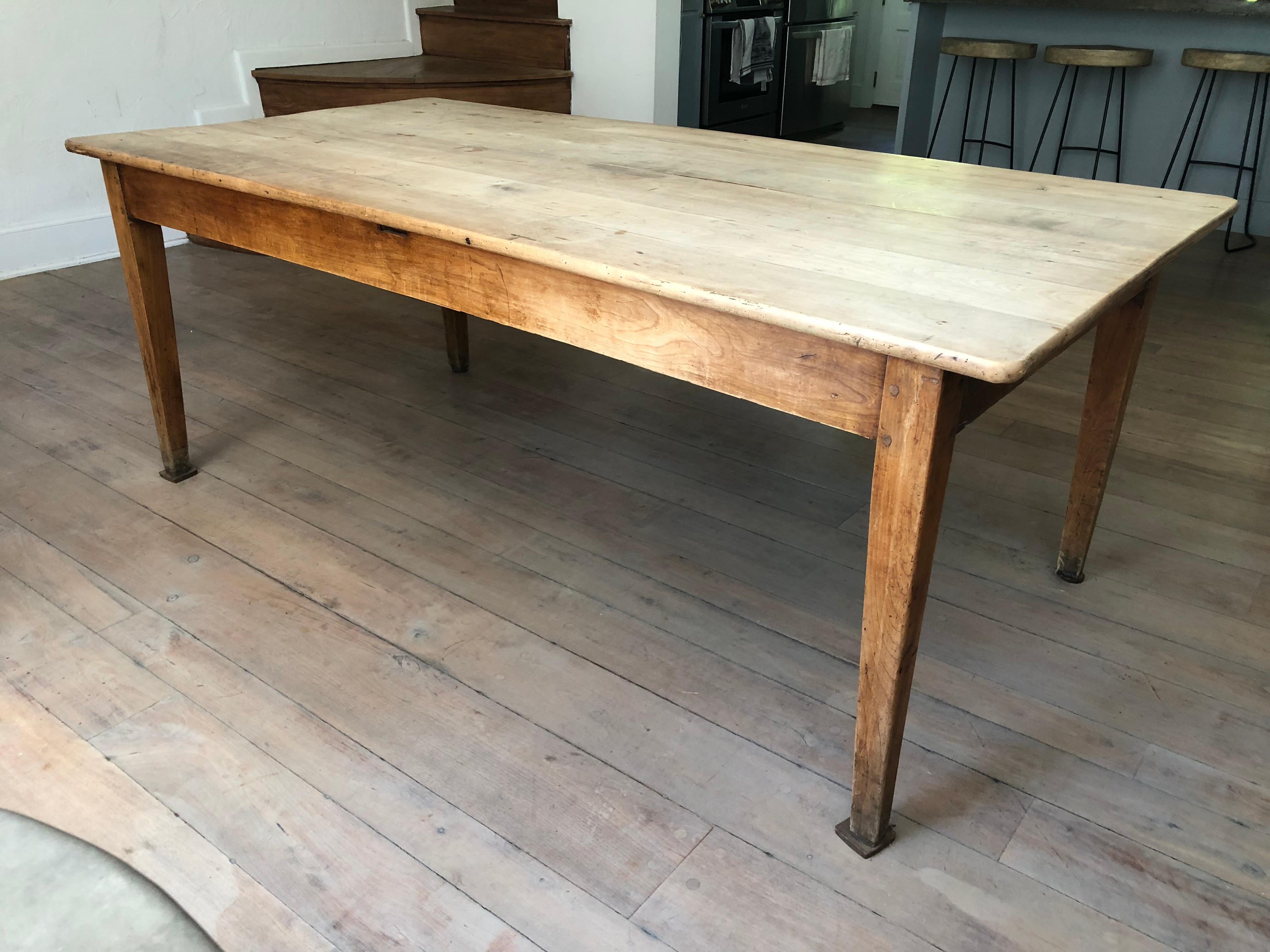 A French Country farm table in bleached cherry, with straight tapered legs, and a large drawer on one end, circa 1800.