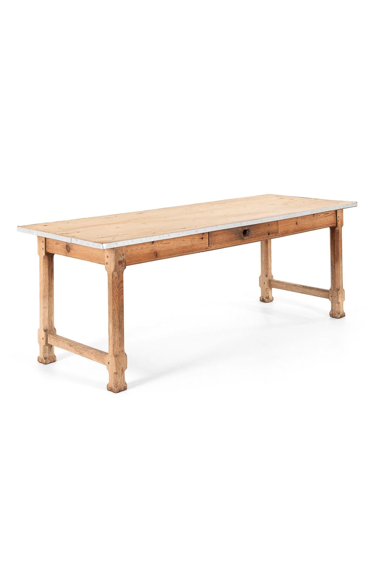 A beautiful provincial farmhouse table with a scrubbed pine top and peripheral aluminium trim.

The fruitwood table base has four carved block legs with cross stretchers, peg and tenon joints and a central frieze drawer.

French, circa