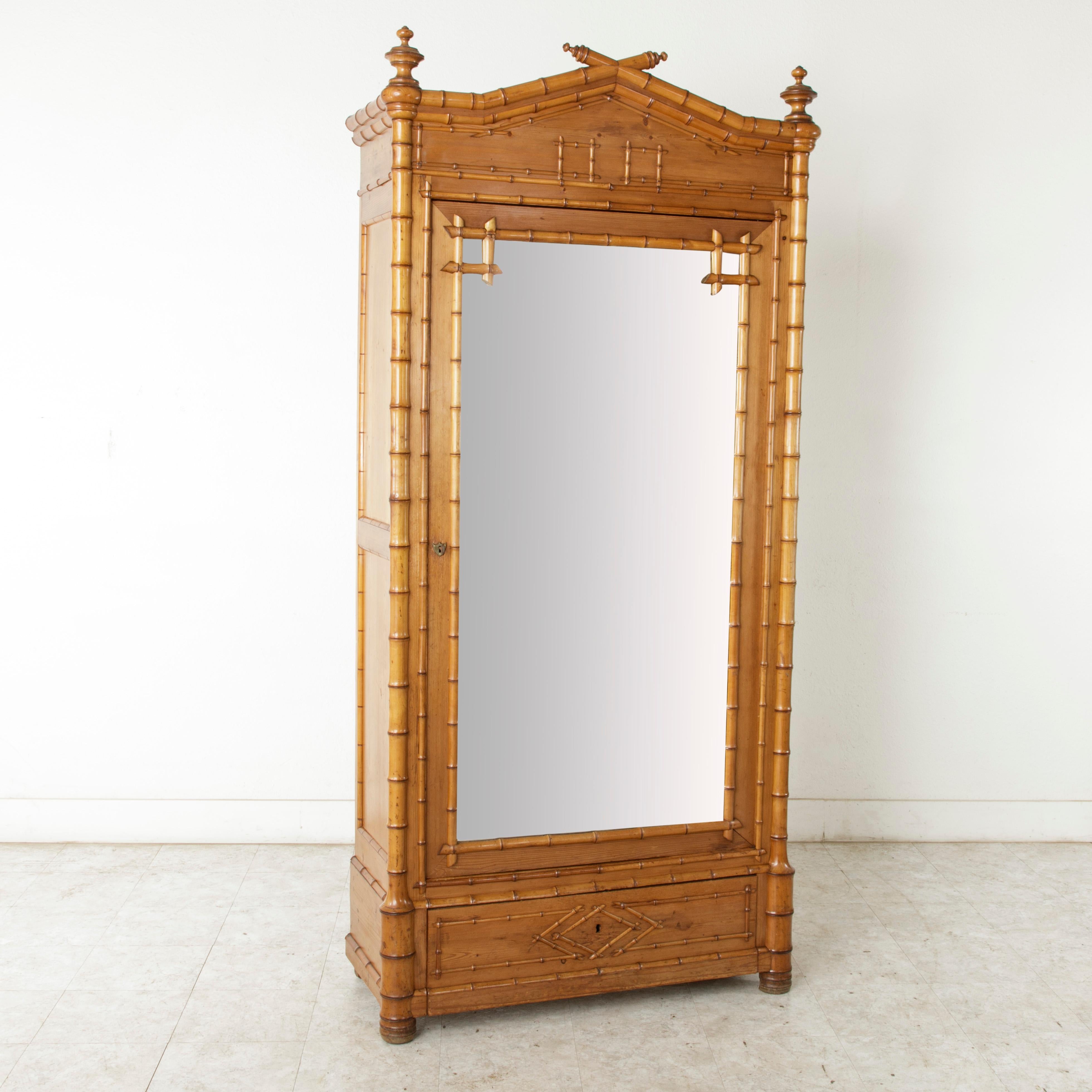 This French faux bamboo armoire is constructed of cherrywood and heartwood pine. Its finely detailed bamboo pieces, harmoniously laid in a uniform pattern, blend with the handsome geometric motif in the upper pediment and lower drawer front.