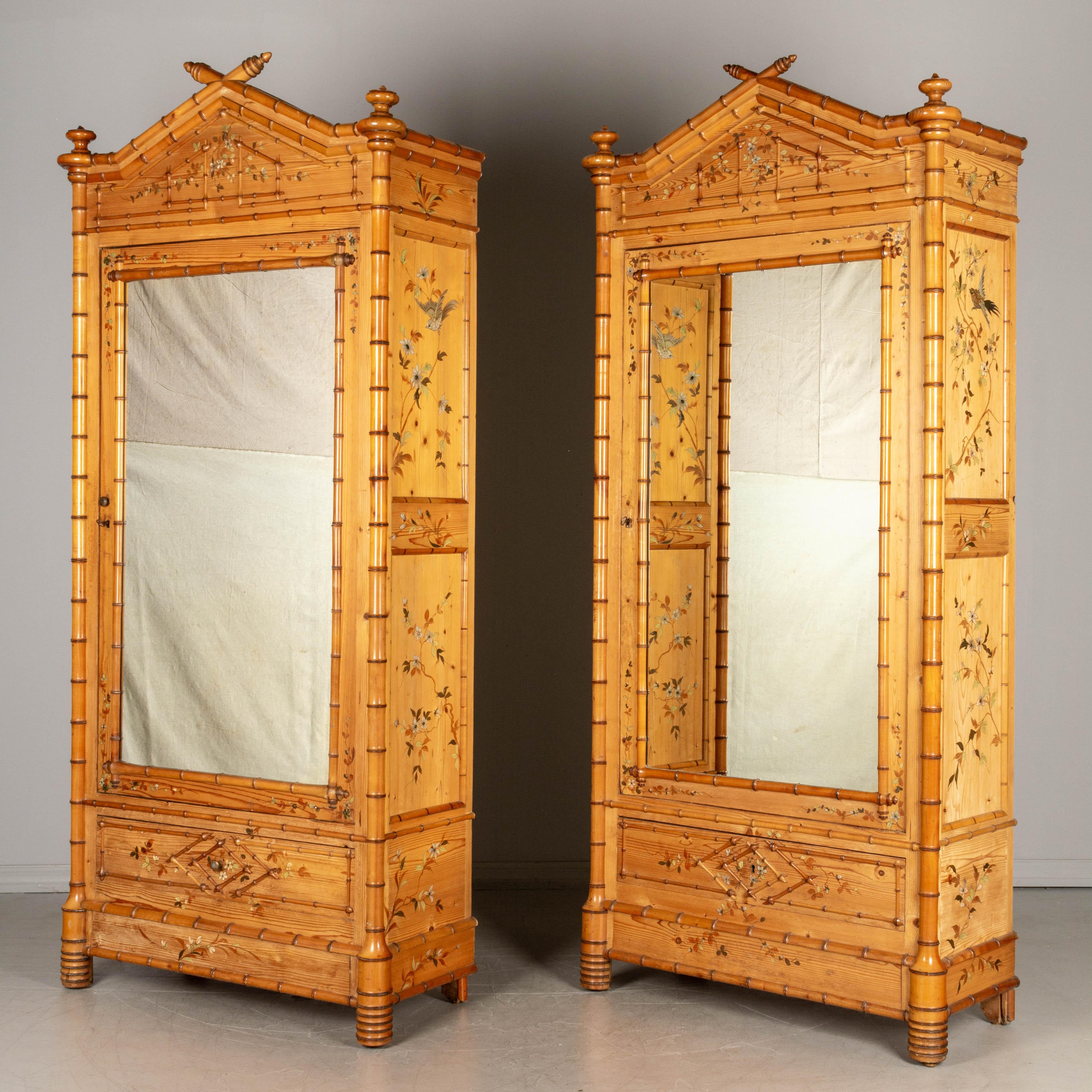 A pair of French faux bamboo armoires, or wardrobes, made of pine with solid cherry faux bamboo details and mirrored door. Hand-painted chinoiserie style decoration: pale green and orange flowering vines and silver birds in raised relief. Turned