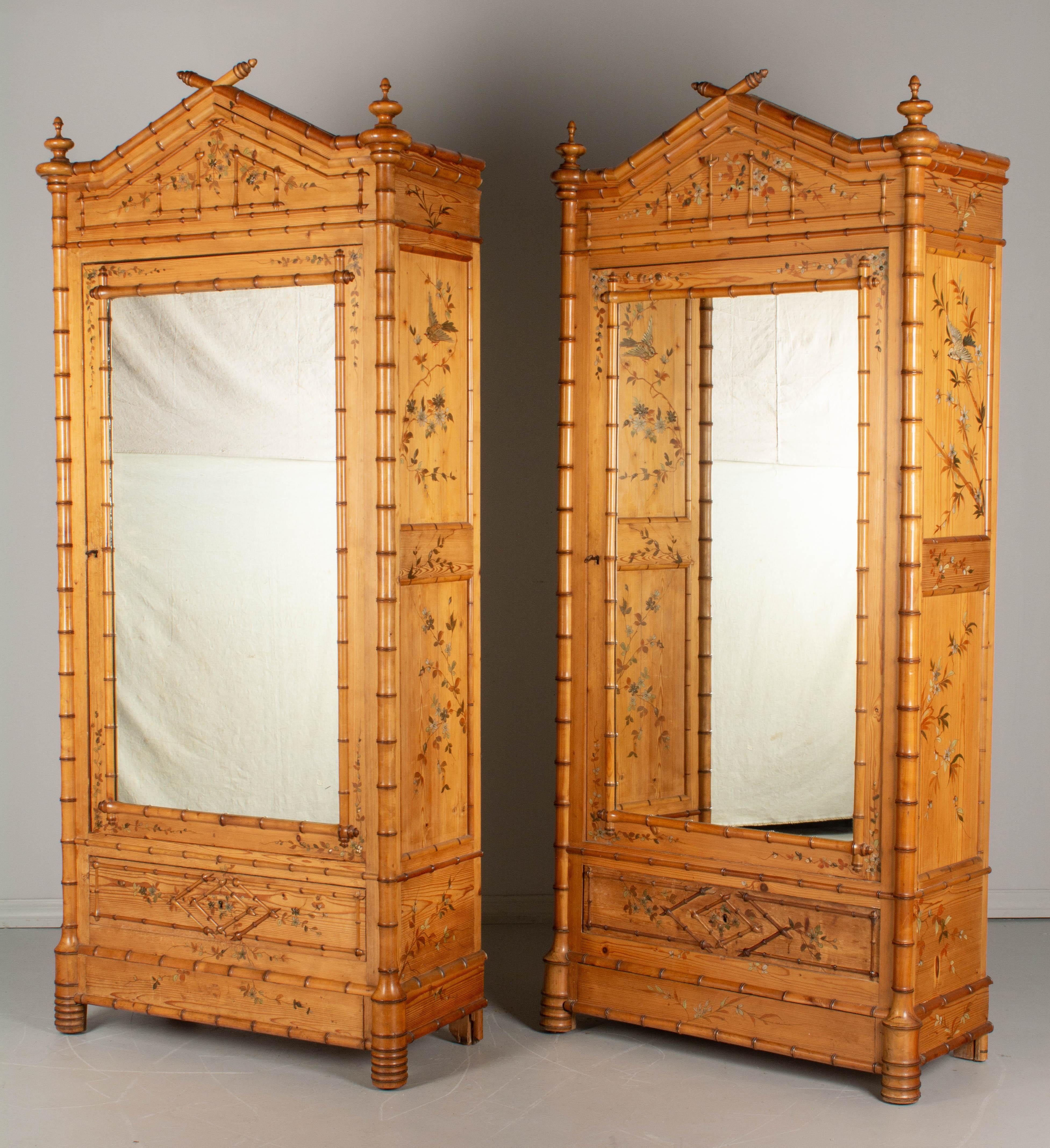 A pair of French faux bamboo armoires, or wardrobes, made of pine with solid cherry faux bamboo details and mirrored door. Hand painted chinoiserie style decoration: pale green and orange flowering vines and silver birds in raised relief. Some paint