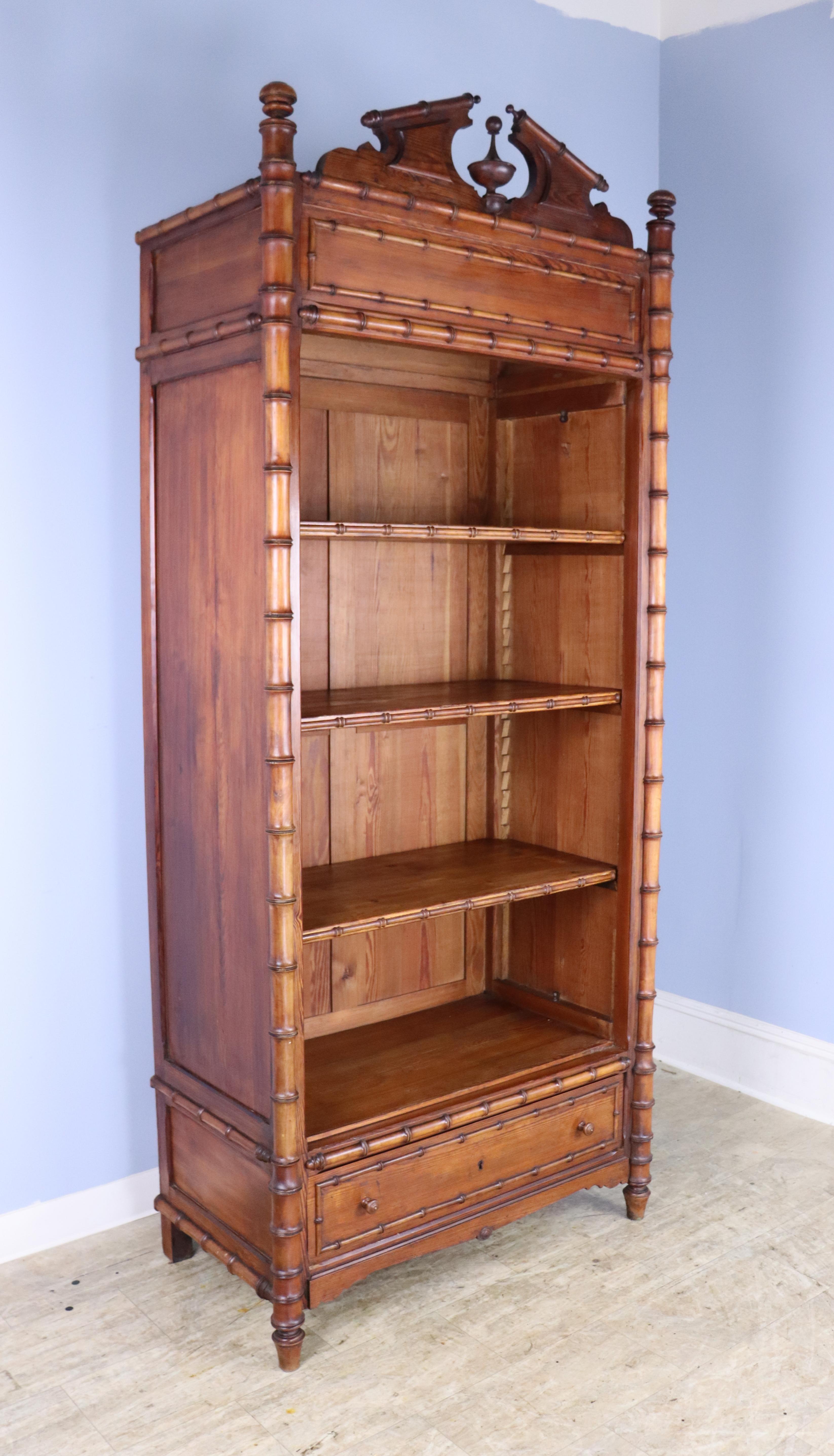 A large and imposing honey colored faux bamboo bookcase from France. The piece boasts three roomy shelves, fully adjustable with a wide bottom drawer. The cornice and lower drawer feature beautifully fashioned wood detail, as do the stylized feet