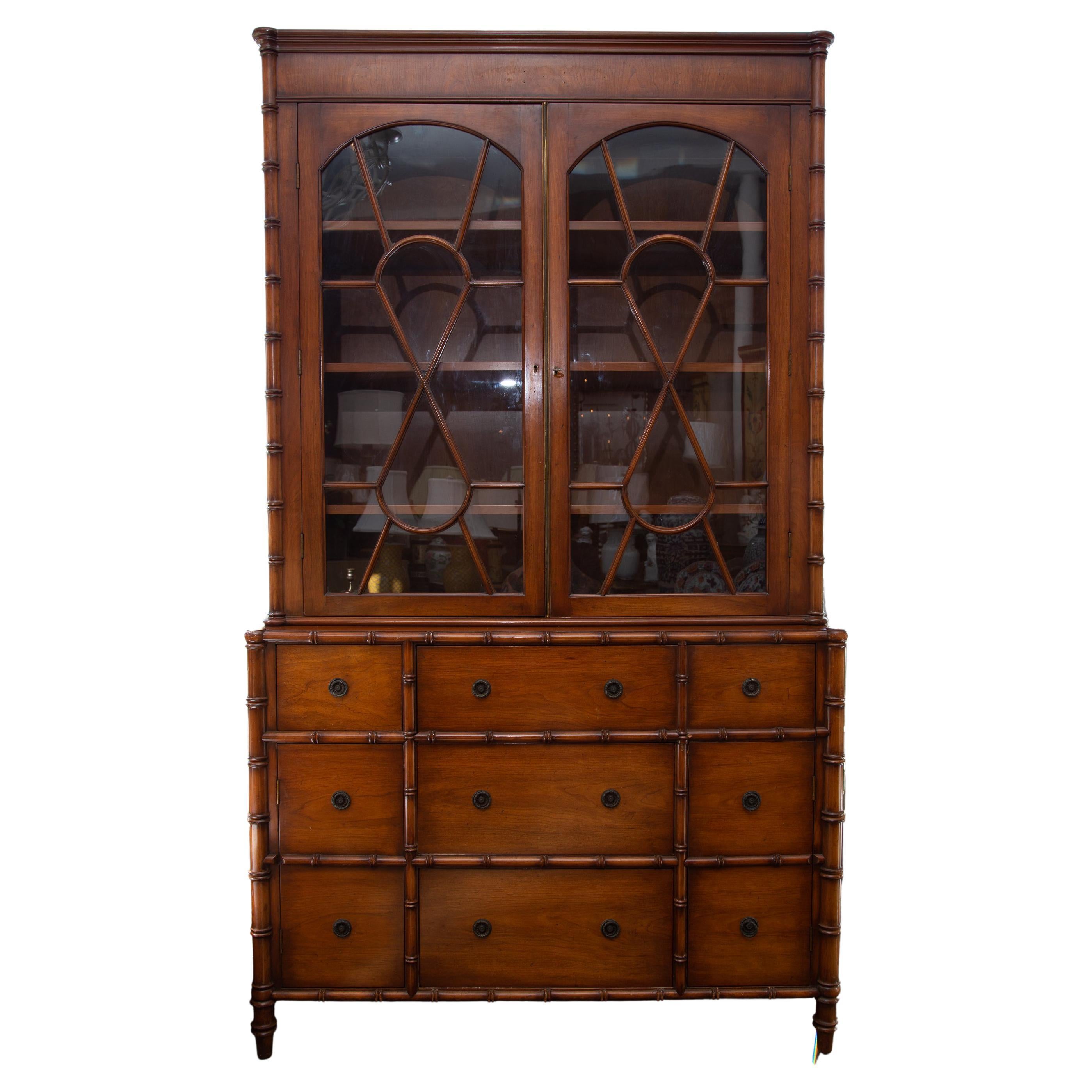 This is a warm, mellow French faux bambooLouis XVI style bookcase/secretaire. The narrow molded cornice and prominent frieze are positioned over two glazed cabinet doors with figure-eight mullions and flanked by faux bamboo corners. The bottom