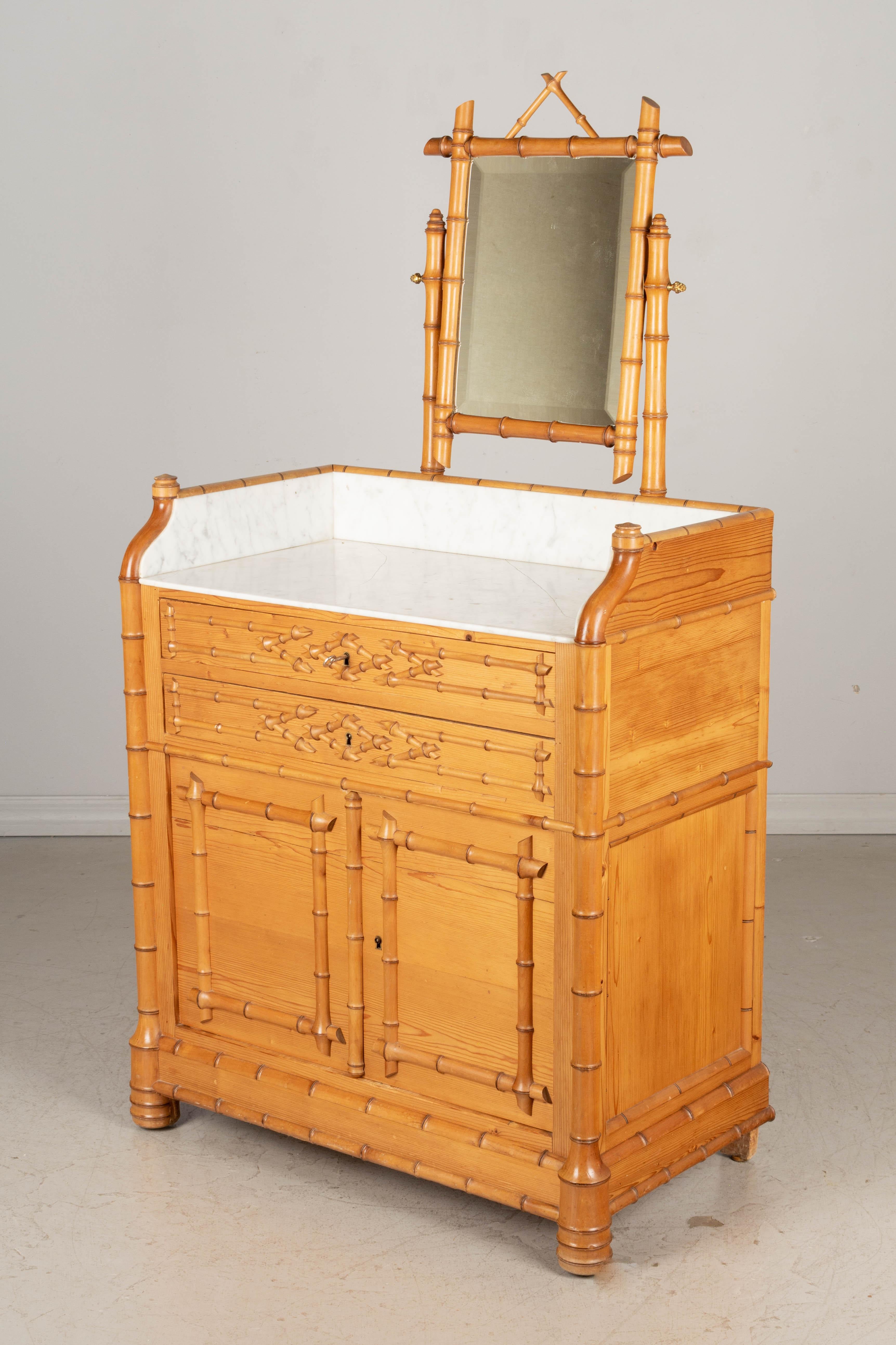 An early 20th century French faux bamboo marble top dresser or wash stand with pivoting vanity mirror. Made of cherry wood with two dovetailed drawers and a cabinet below, each with working locks and one key. White marble top (16.5