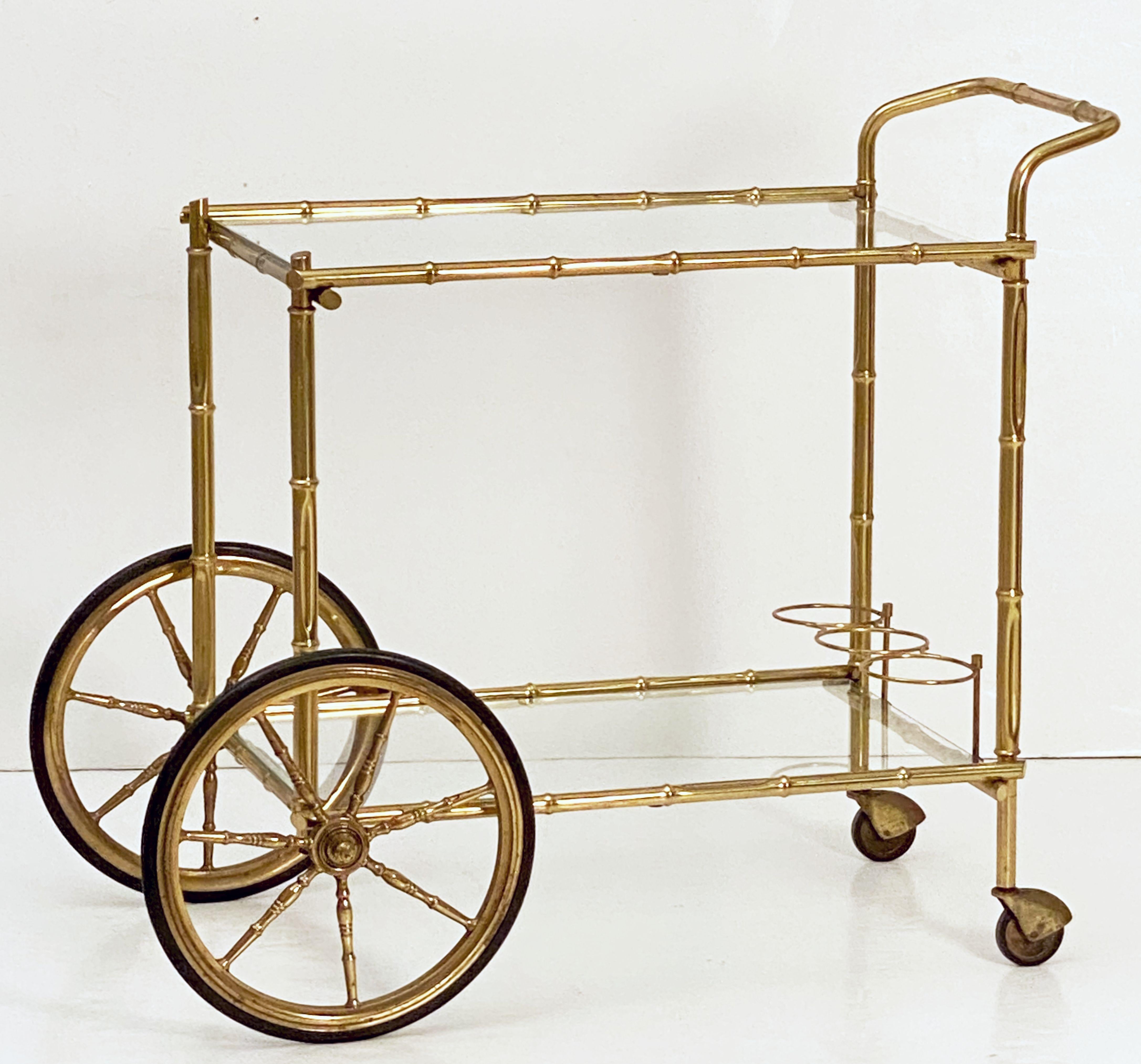 A handsome vintage French rectangular bar cart table or serving trolley in brass, featuring two glass tiers, with bottle rack on bottom tier, resting on rolling caster wheels. The larger back two wheels with a spoked design.

Perfect for use as a
