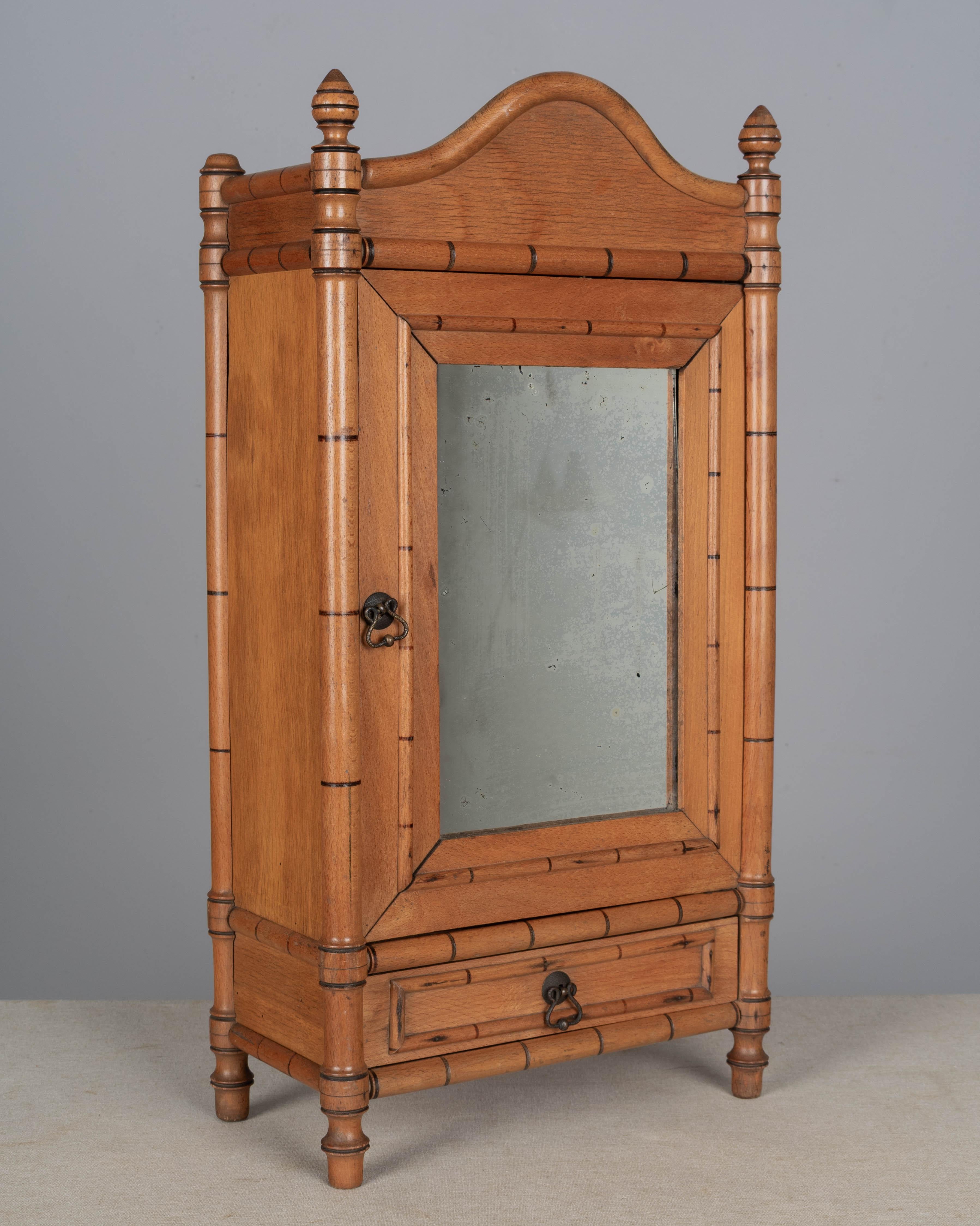 A French faux bamboo miniature armoire made of beech and pine with mirrored door and small drawer. Nicely detailed with turned trim and finials. Interior has two shelves. May be used as a wall hung medicine cabinet, or spice rack. Original mirror