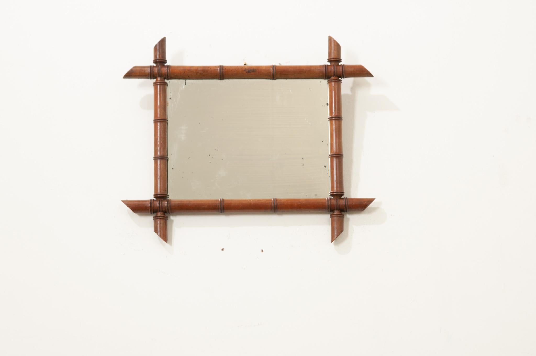 A French vintage rectangular faux-bamboo mirror from the 20th century, with a lovely honey brown patina. This simple mirror features a rectangular Silhouette made of a carved faux bamboo frame showcasing intersecting corners. This mirror charms us