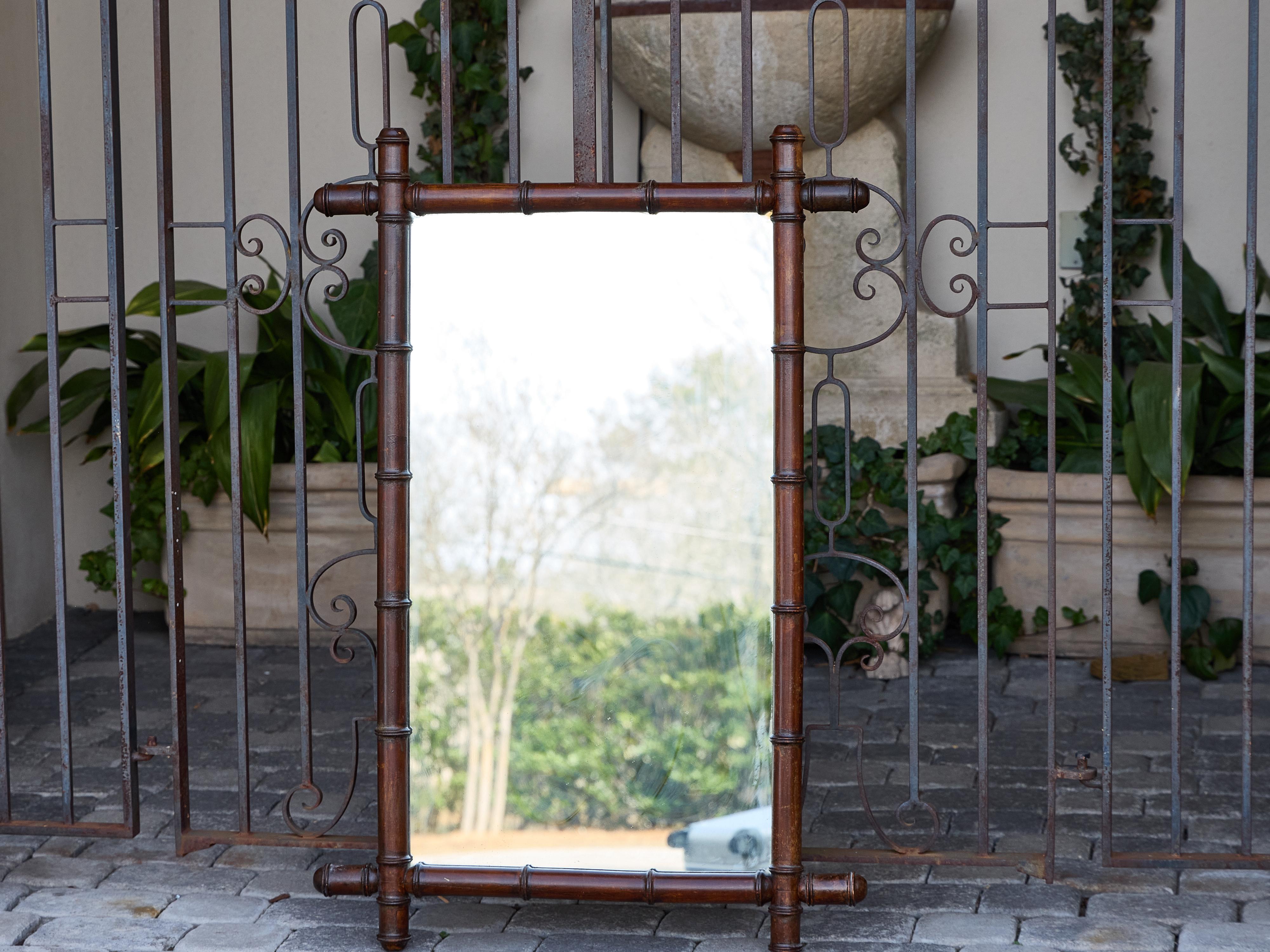 Questo specchio francese in finto bambù del 1900 circa offre una visione calda e scultorea del design della fine del XIX secolo. Realizzata in legno intagliato e rifinita con una ricca tinta marrone-rossastra, la cornice imita in modo convincente