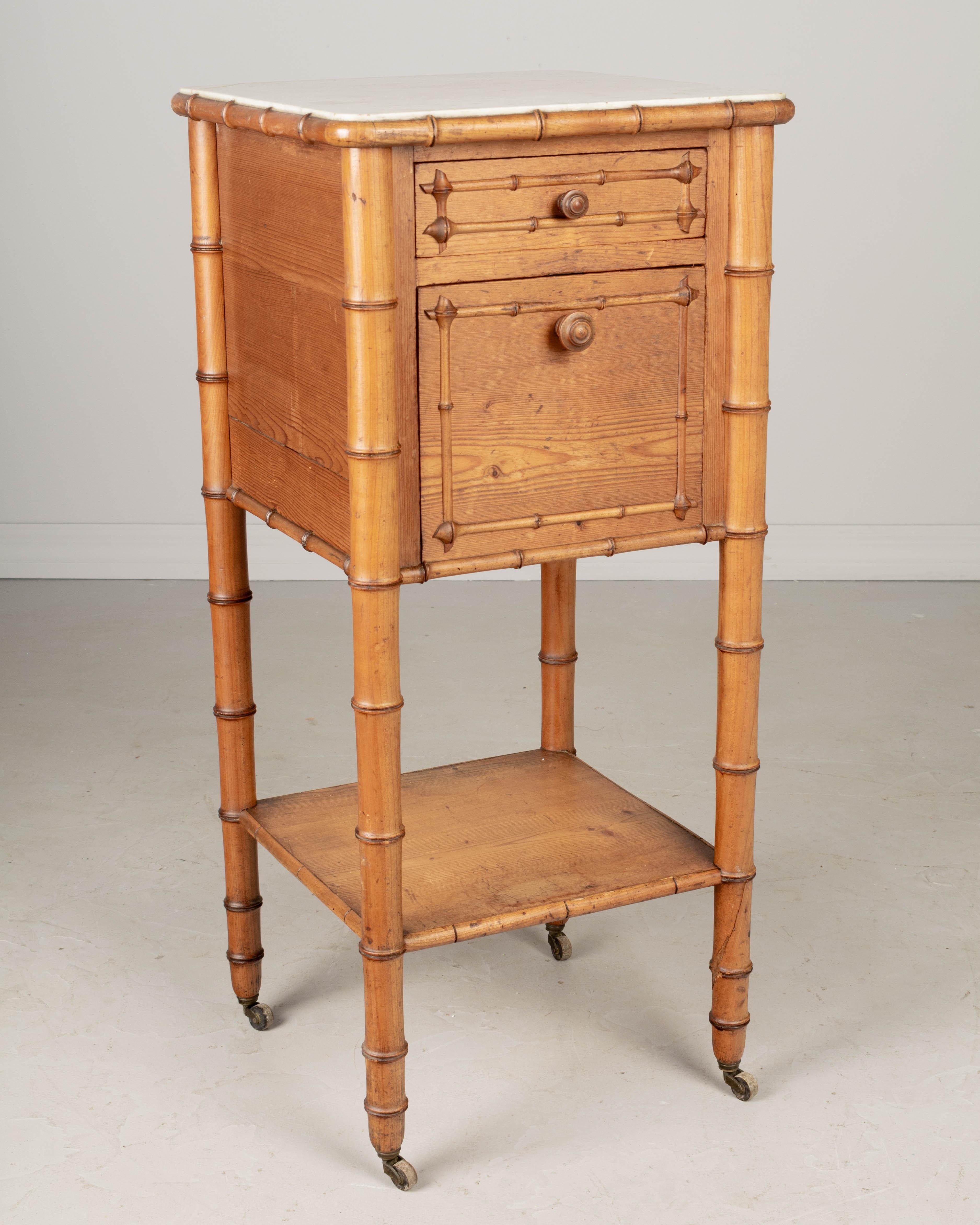 A 19th century French faux bamboo marble top bedside table, or nightstand made of pine. Dovetailed drawer and a door that hinges open to reveal a marble lined interior compartment. Turned legs with castors. Inset white marble top with curved