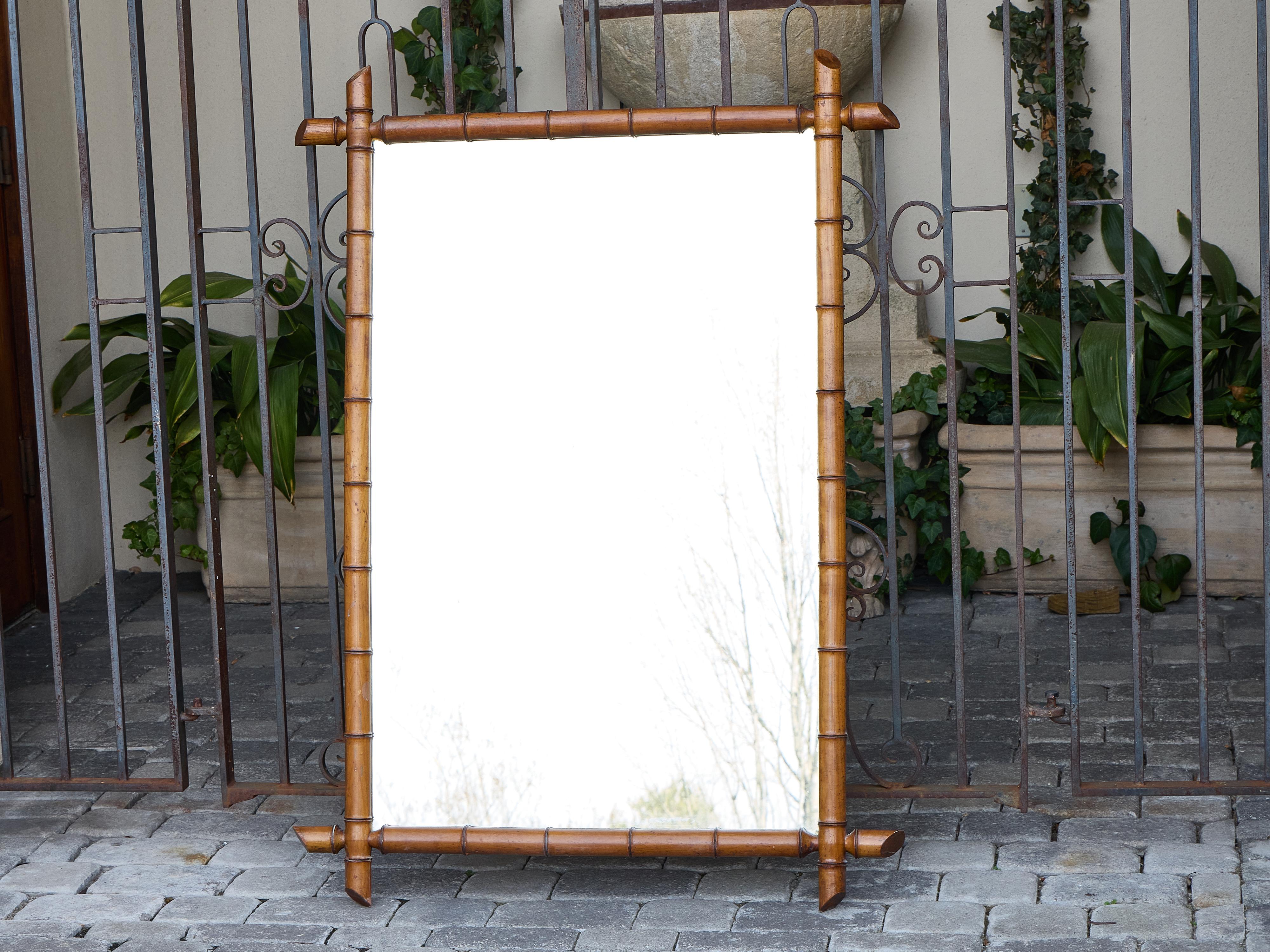 This French faux bamboo mirror dates to circa 1920 and captures the tailored, worldly charm of early 20th-century colonial revival design. Framed in turned and carved wood finished to emulate bamboo, it offers a warm honeyed tone with subtle reddish