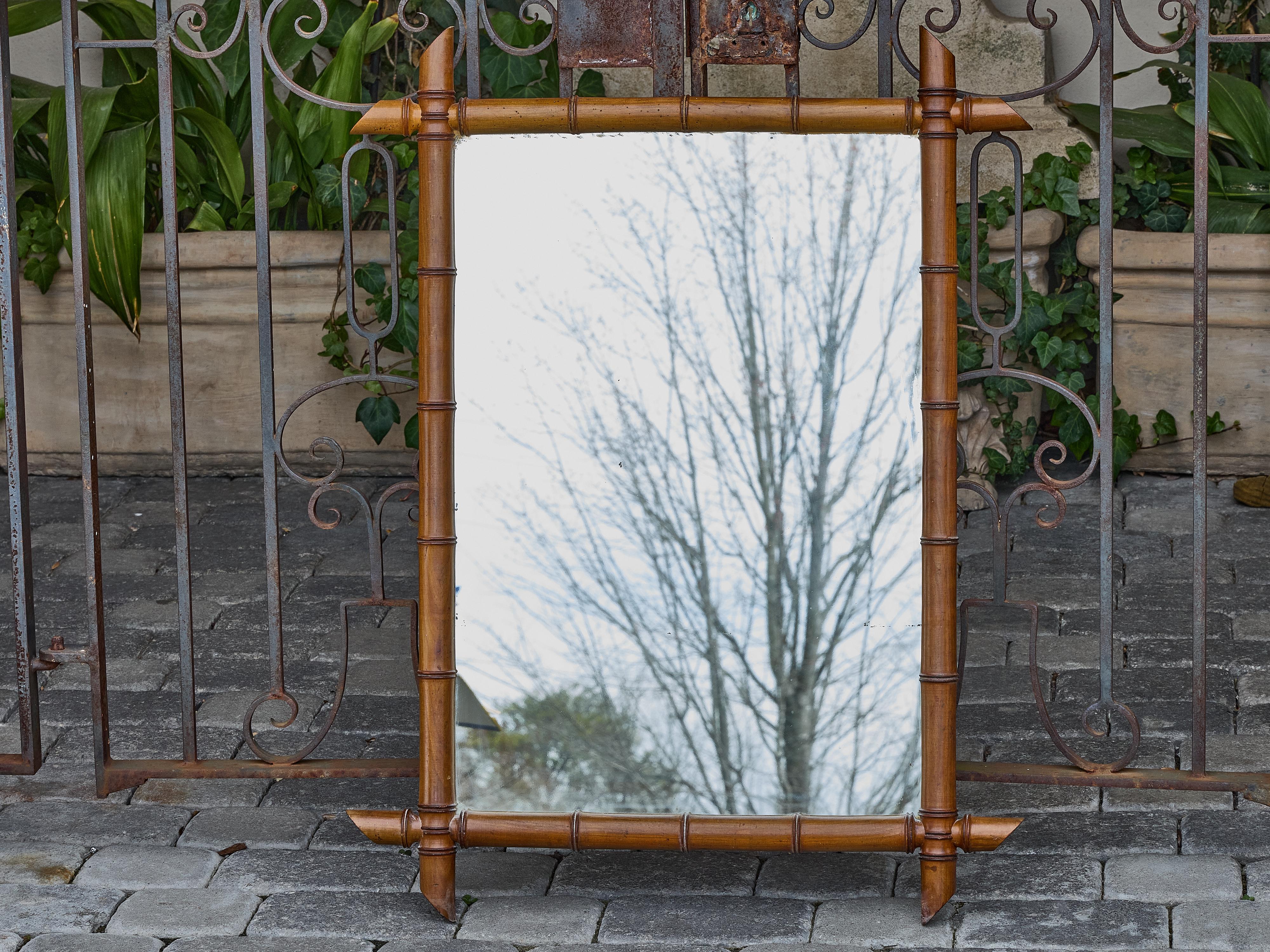 A French faux bamboo mirror from circa 1900, carved from solid wood and finished in a mellow honey tone that highlights its turn-of-the-century charm. The rectangular frame is styled to resemble bamboo, complete with segmented detailing and extended