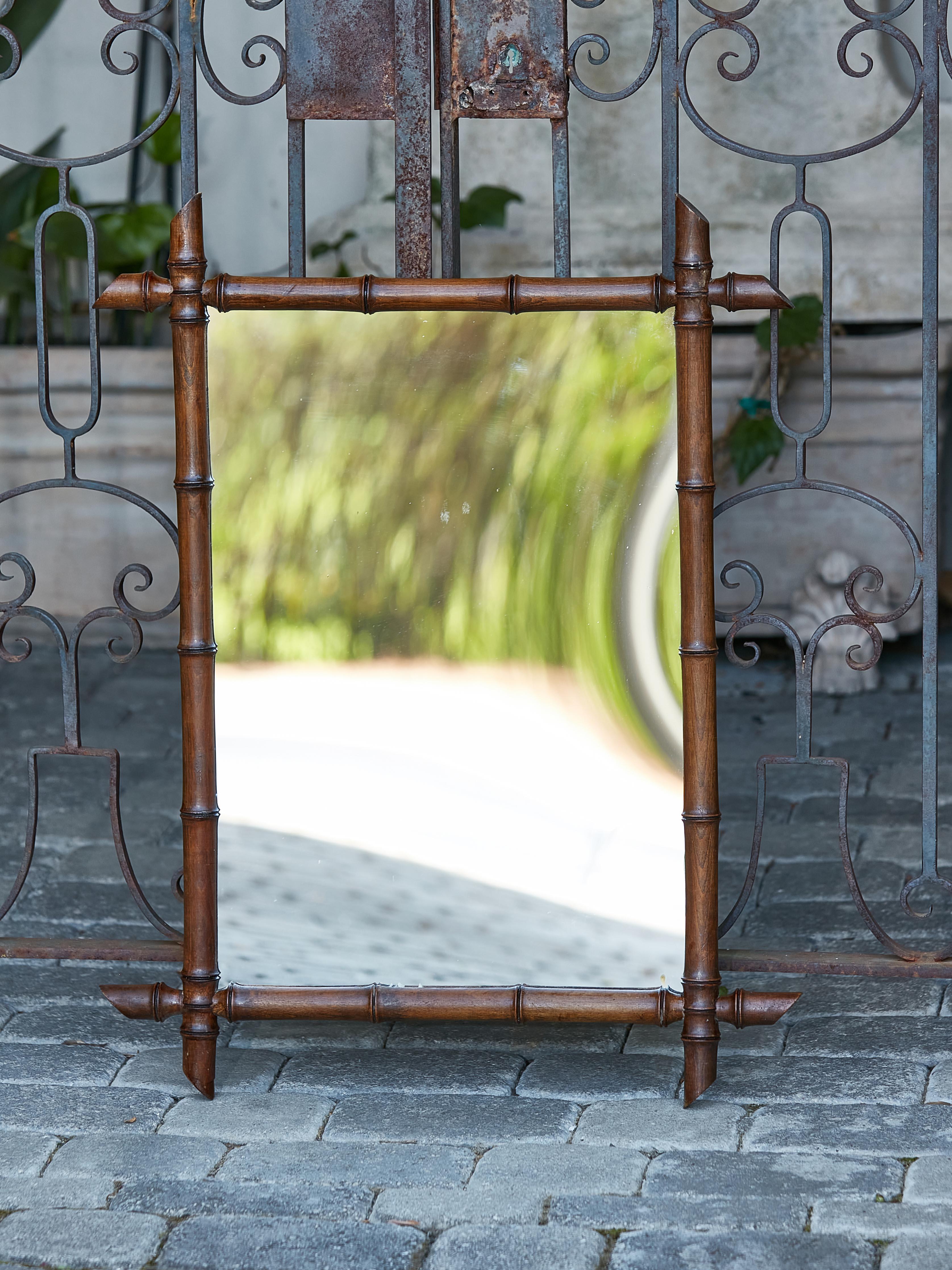 A French turn of the century faux-bamboo mirror from circa 1900 with intersecting corners, slanted accents and dark brown patina. Introducing a French Turn of the Century faux-bamboo mirror that effortlessly fuses rustic charm with elegant artistry.