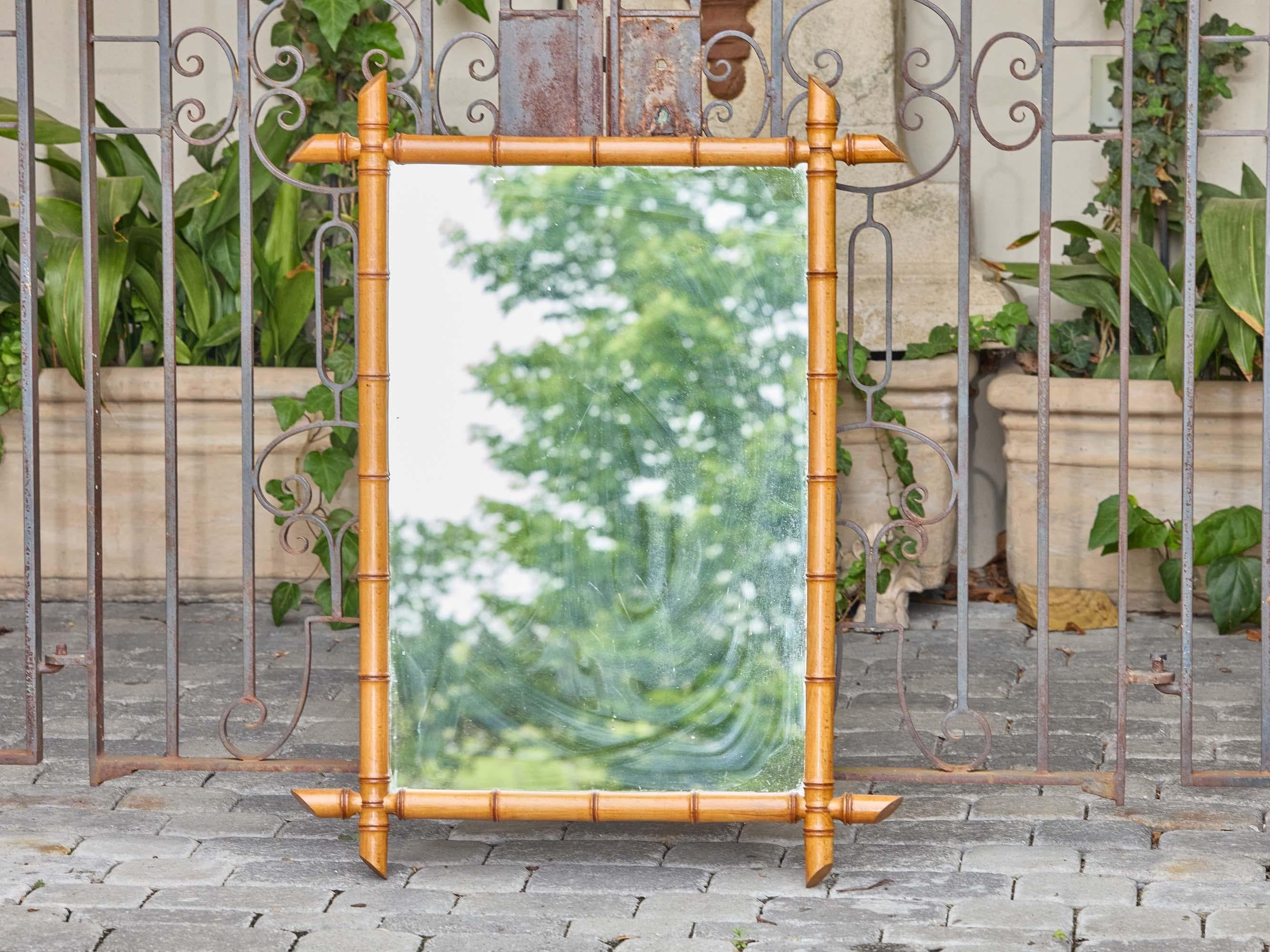 Questo specchio da parete in finto bambù francese del 1900 circa cattura il fascino e la leggerezza associati alle decorazioni in legno di fine secolo. La cornice è realizzata in legno intagliato e tornito, modellato per imitare il ritmo segmentato