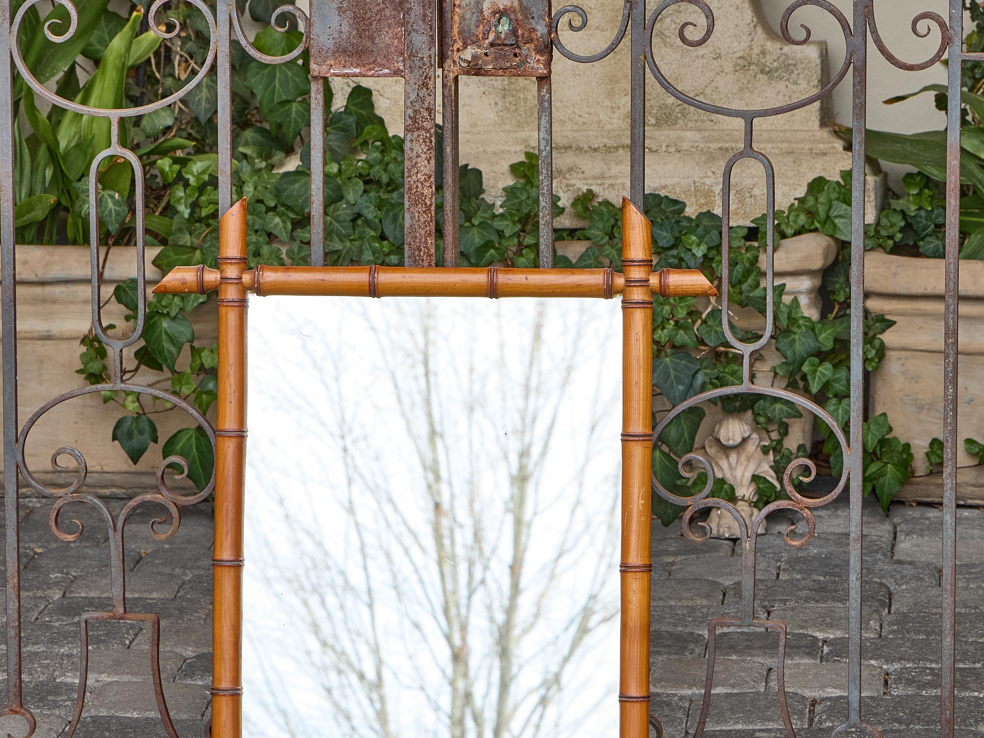 Fabriqué en France au début du XXe siècle, ce miroir en faux bambou capture l'attrait durable des styles exotiques qui ont fleuri à la fin du XIXe siècle. Le cadre en bois de couleur miel chaud a été soigneusement tourné et sculpté pour imiter les
