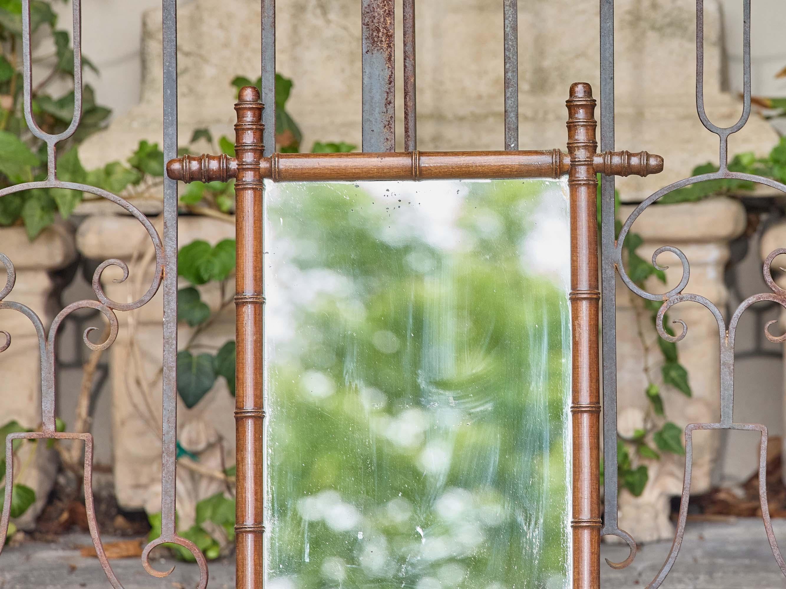 Specchio da parete in finto bambù francese del 1900 circa con finitura marrone caldo e caratteristici pioli torniti agli angoli. La cornice presenta un classico intaglio in finto bambù, tipico del gusto del tardo XIX e dell'inizio del XX secolo per