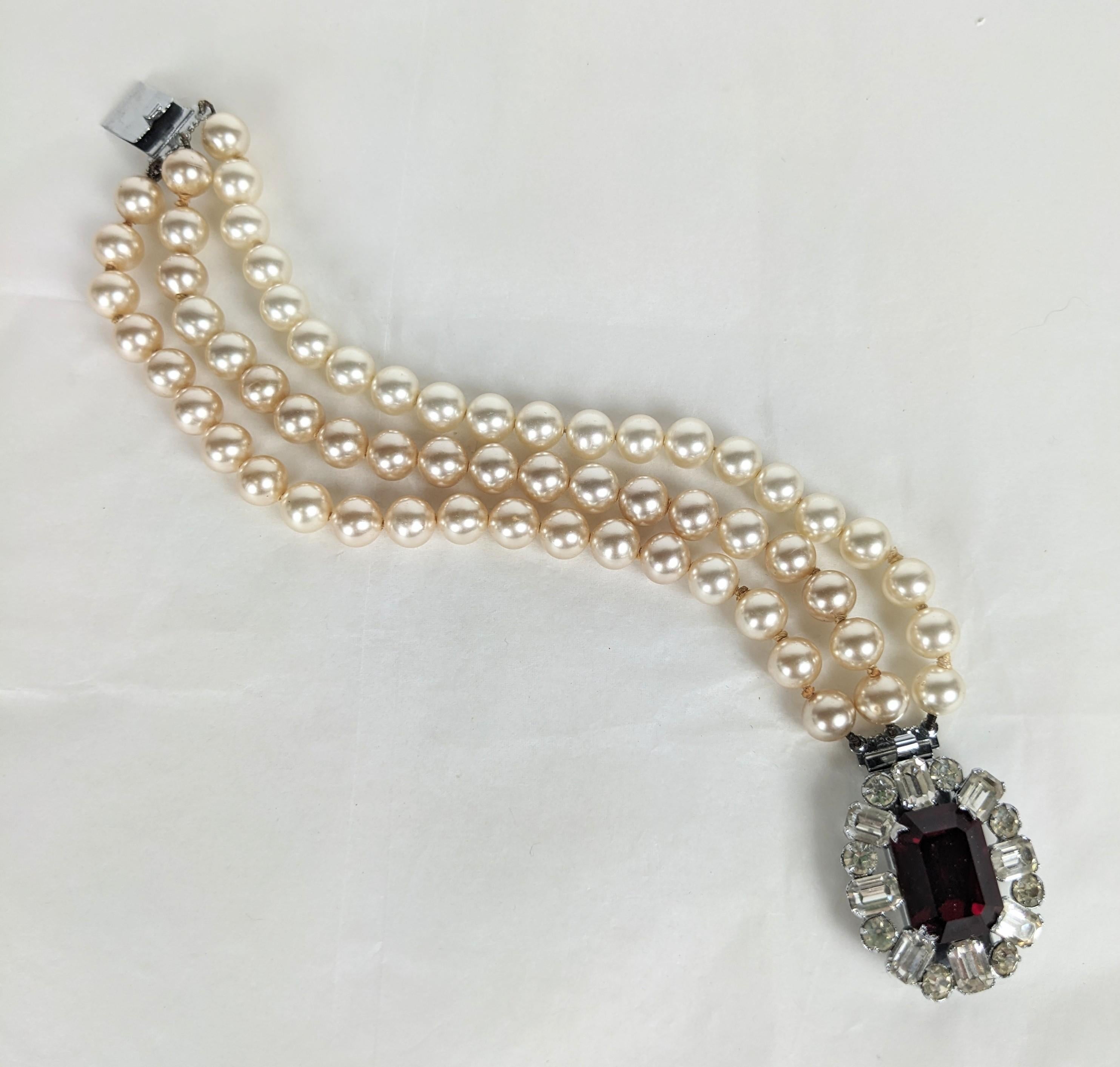 Elegant French Faux Pearl and Ruby Clasp Bracelet from the 1950's. 
3 strand faux pearls with large ruby paste and crystal clasp. Hand knotted and bullioned like fine jewelry. 1950's France. 
Clasp 1.5