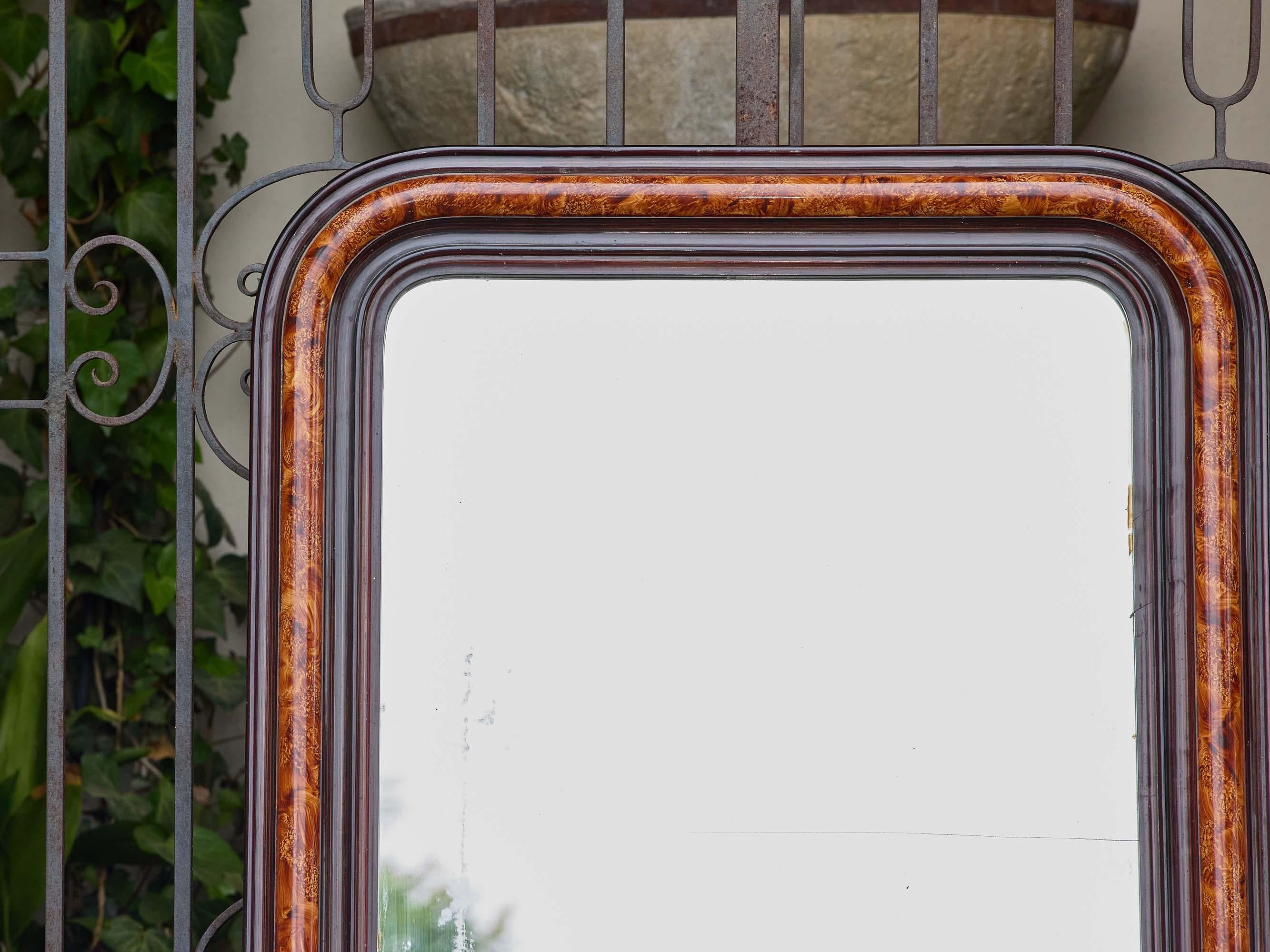 A French Louis-Philippe style mirror from circa 1920 featuring a richly colored faux tortoiseshell frame with rounded upper corners and a contrasting ebonized inner molding. The frame’s warm amber and dark brown tones emulate natural tortoiseshell,