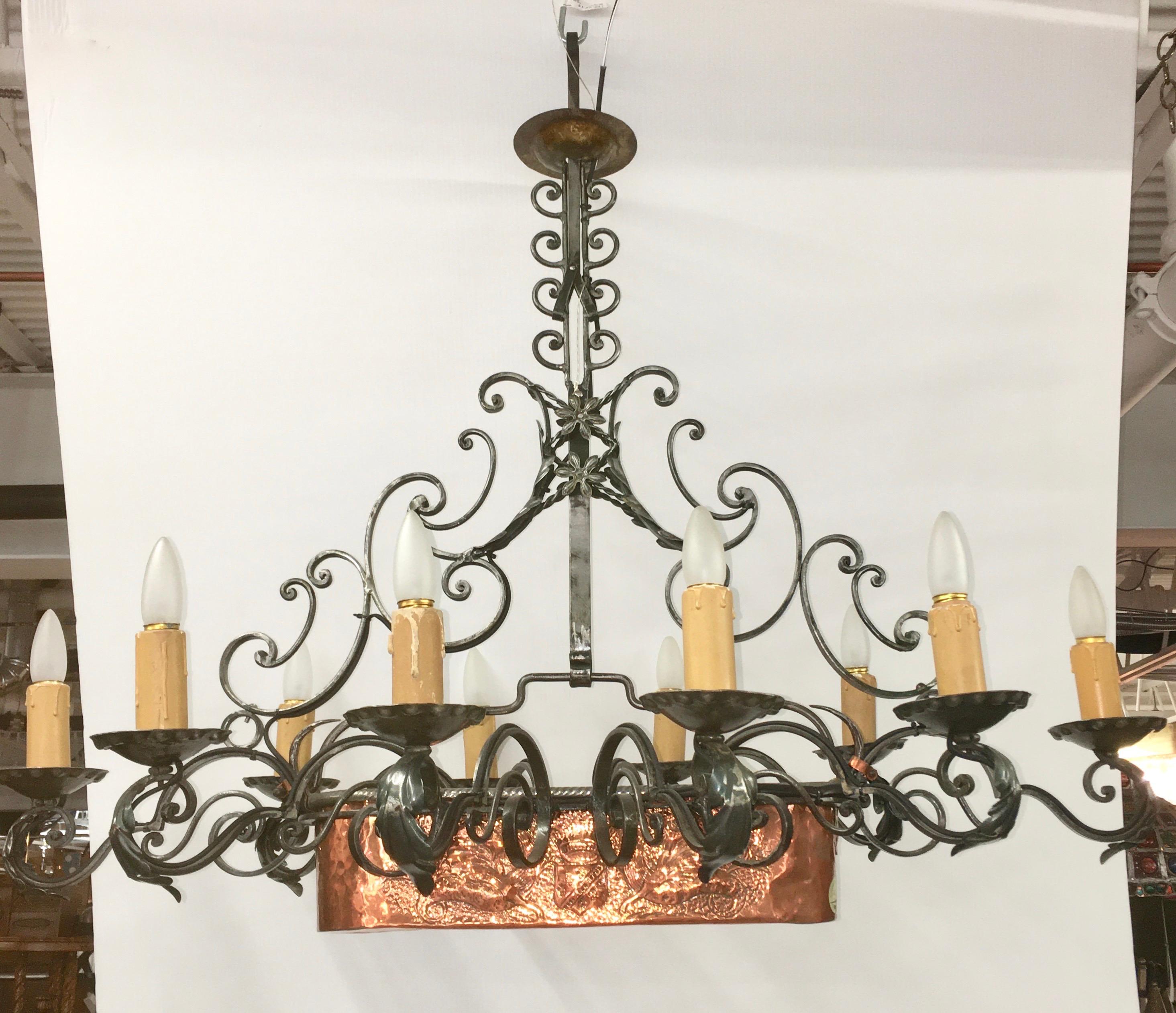 Beautifully handcrafted wrought iron chandelier on a linear rectangular axis having ten lights around a fixed central planter of hand hammered copper with repousse designs of flowers on one side and the crest and shield of a noble family on the