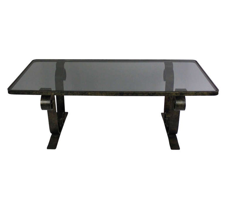 A French fer forge occasional table with scrolled ends, patinated and with a smokey grey inset glass top.