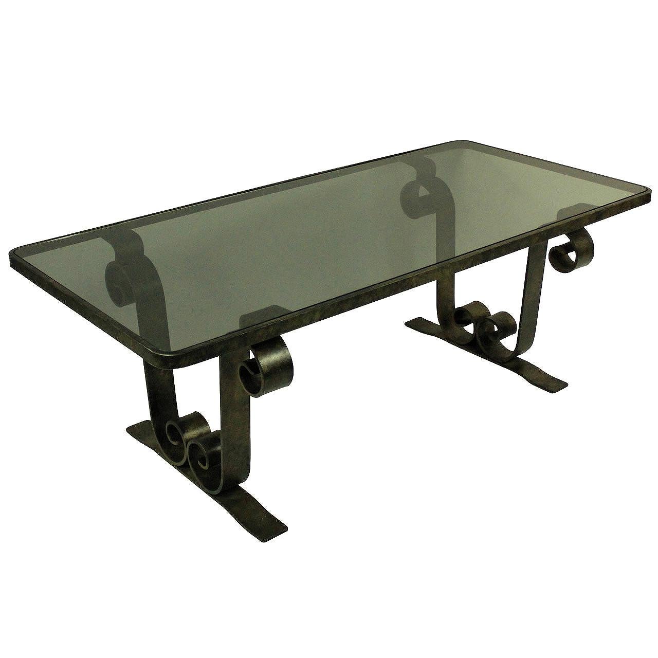 A French fer forge occasional table with scrolled ends, patinated and with a smokey grey inset glass top.