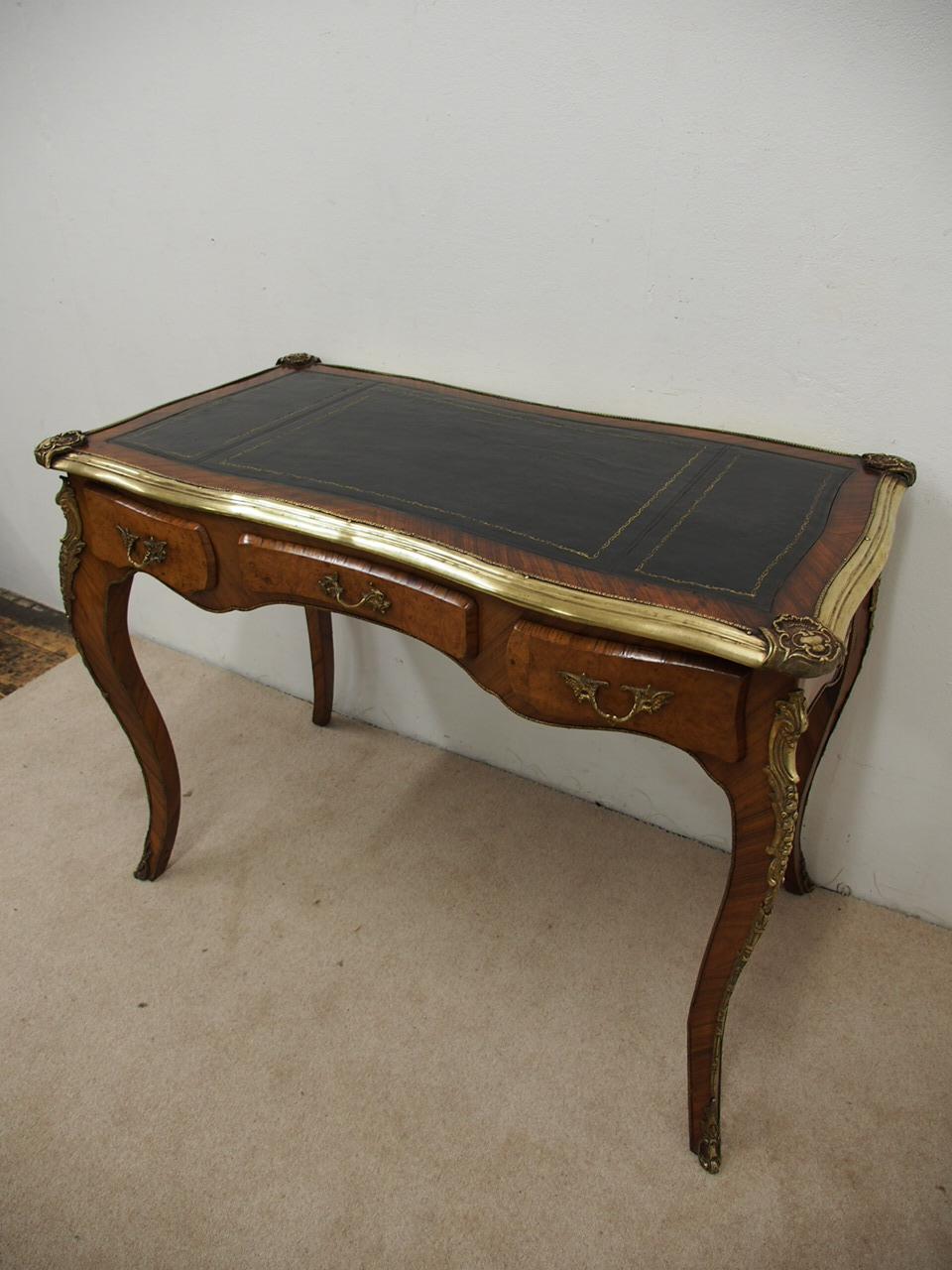 Neat sized French figured walnut serpentine-front, writing table, circa 1900. With extensive brass mountings including brass mouldings around the top and figured walnut banding, a gilt tool and dark coloured skiver that is in excellent condition.