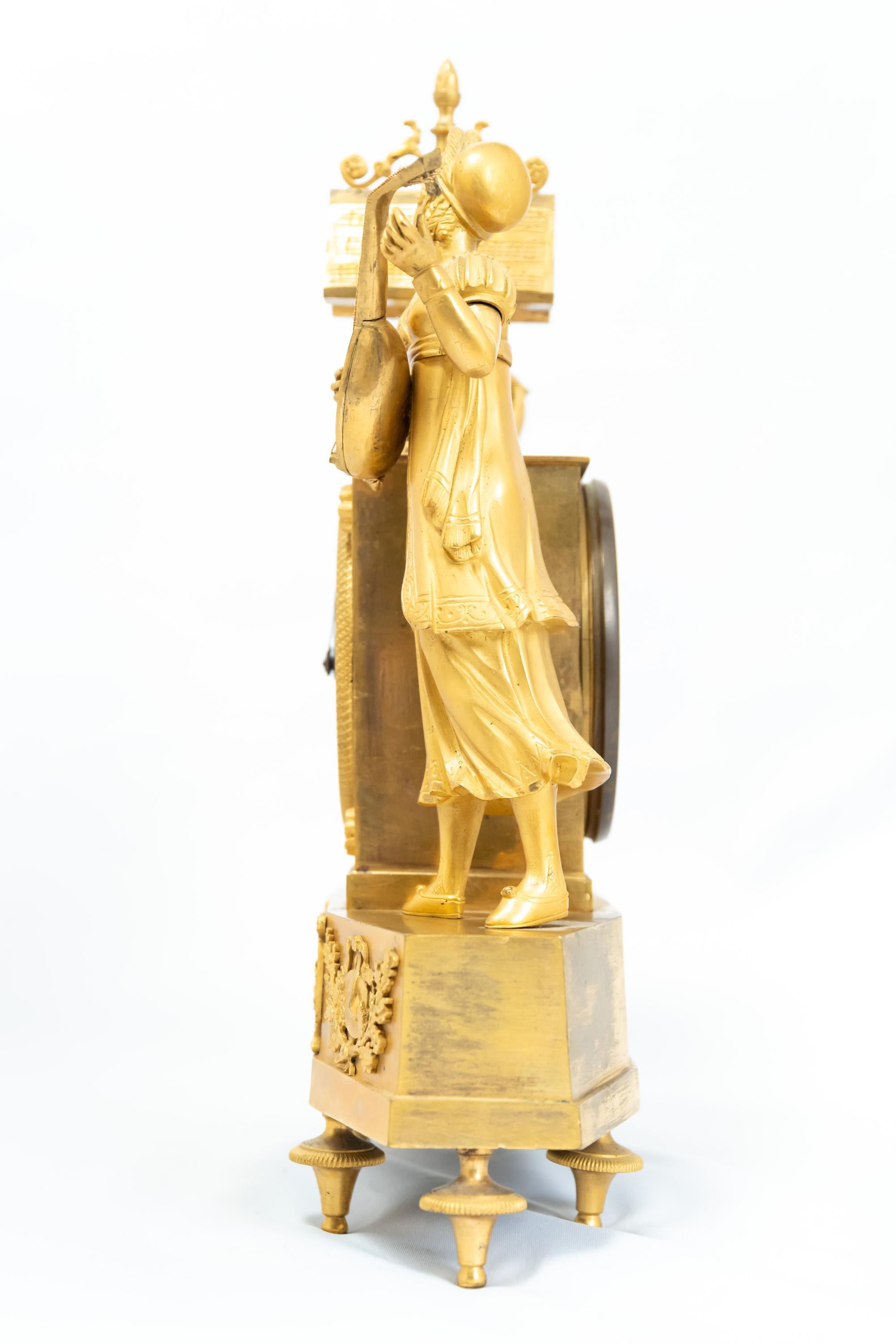 A French fire-gilt clock depicting a standing pair of figures in “troubadour” attire, Restauration Era, 1815-1830. The silk-thread mechanism is in good working condition with key and pendulum.
