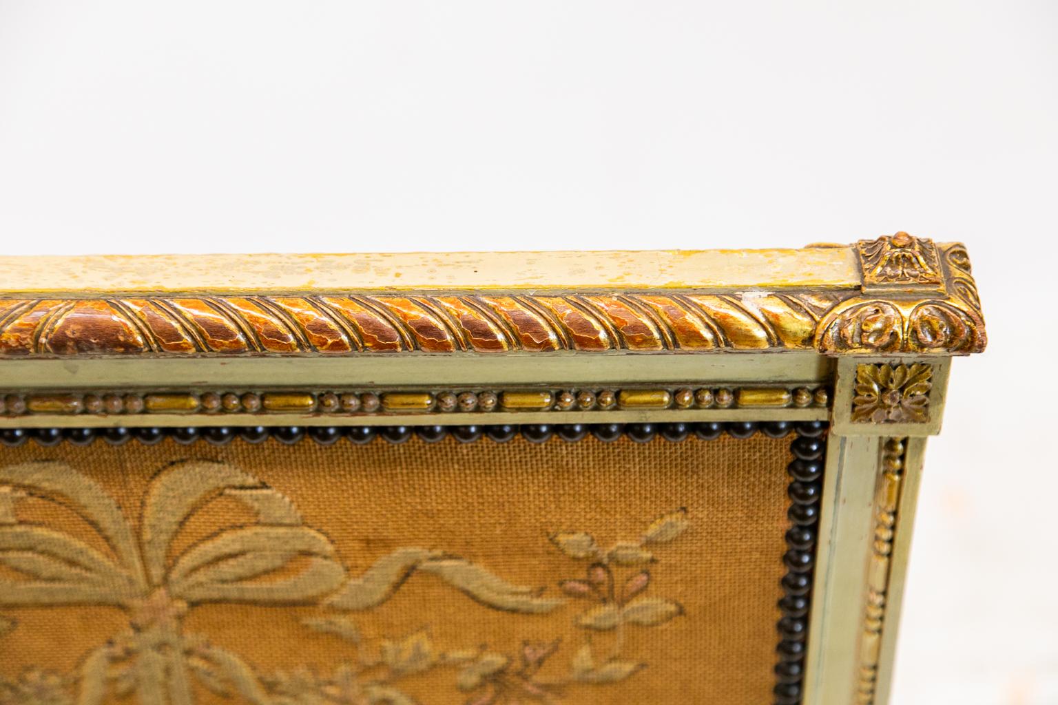 The frame of this French fire screen is painted with a cream color and has a carved gilt gadrooned top rail. The center needlework panel is framed with molding and carved ball and capsule molding. The center is lined with brass stud work.
  