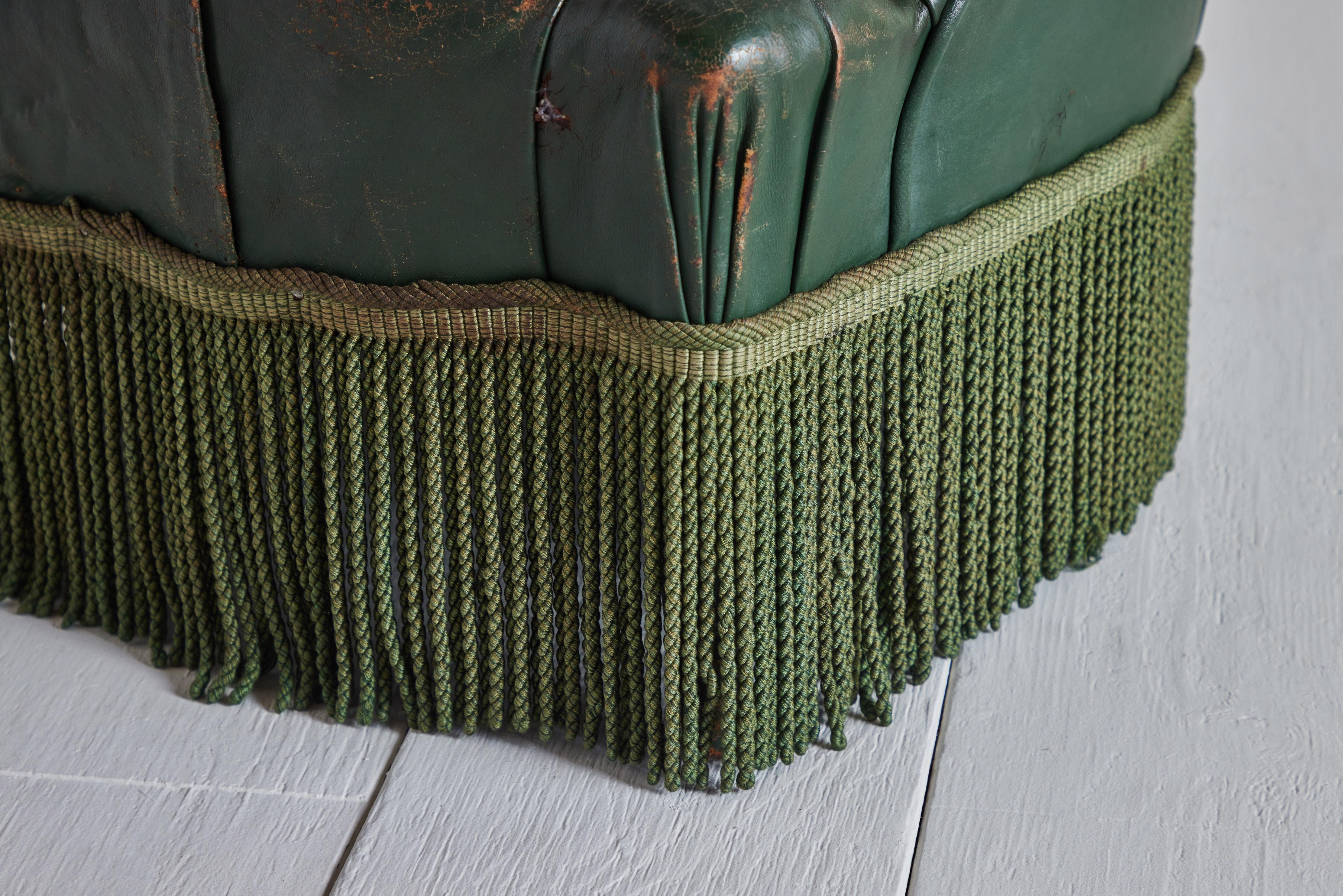 Green tufted leather and silk fringe fireside chair from France circa 1900. Leather has heavy wear that is consistent with age and use.