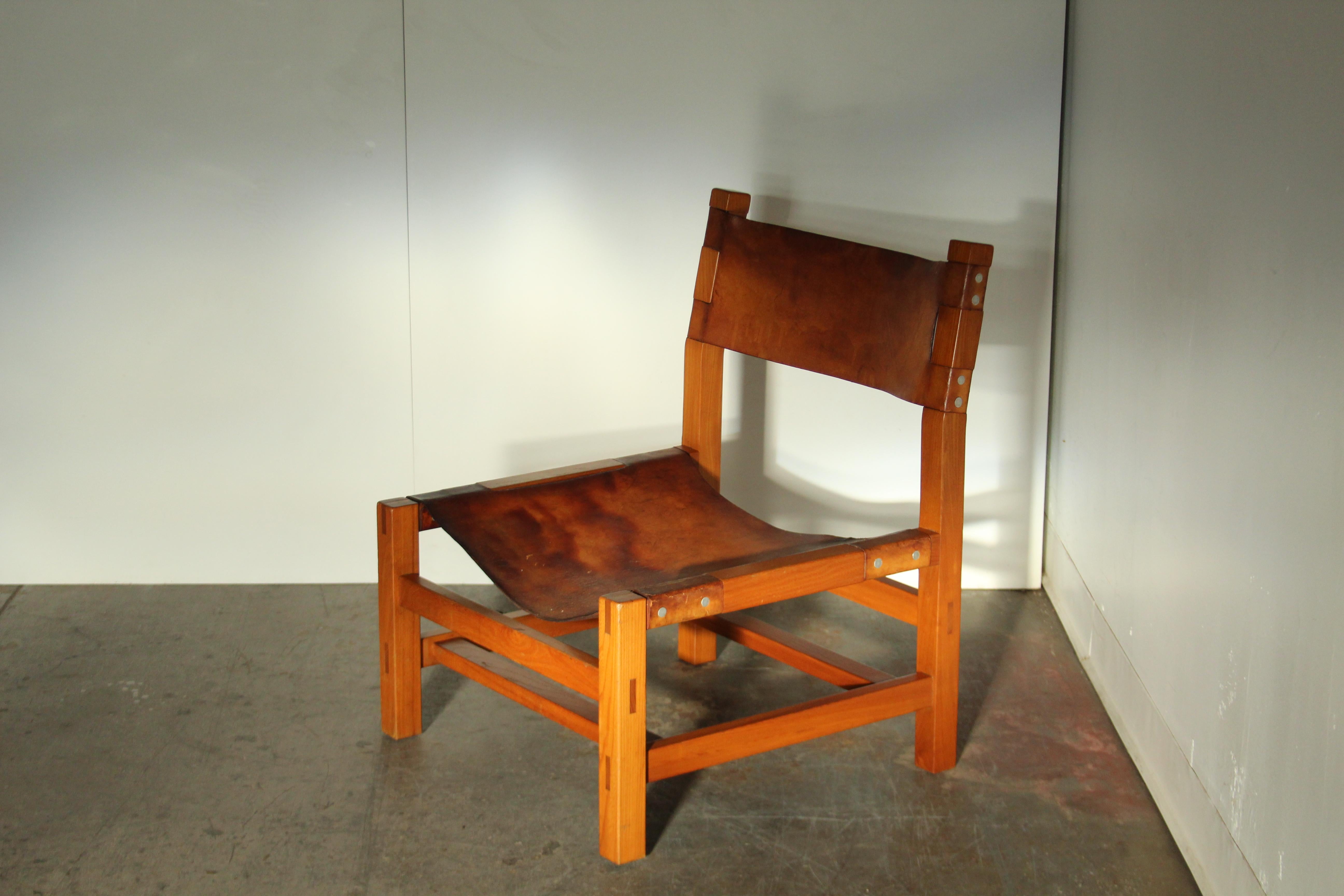 A stunning French fireside lounge chair produced in the 1970s, attributed to Maison Regain. Simplistic angular form with sophisticated wood joinery and amazing inset leather detailing. Solid elm frame. The original leather shows tons of patina. The