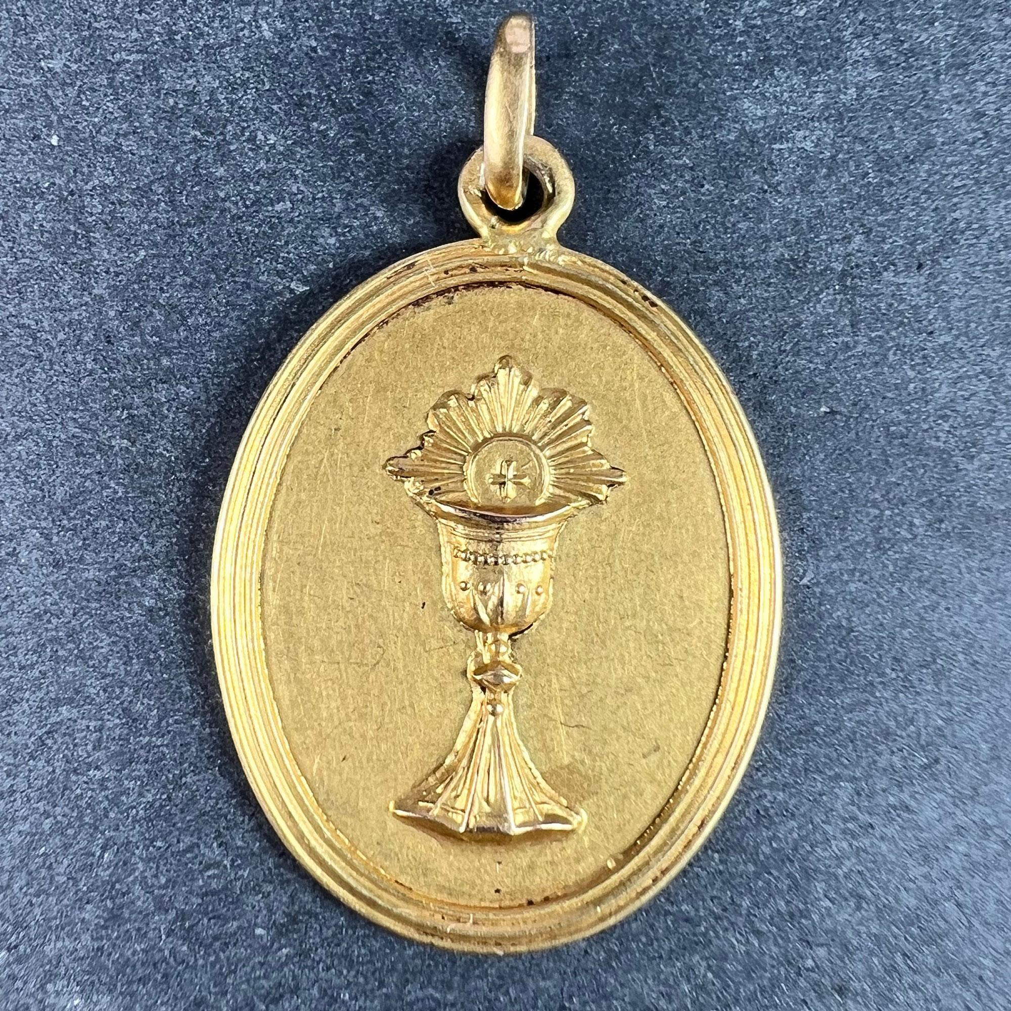 A French 18 karat (18K) yellow gold charm pendant depicting a chalice surmounted with a wafer, representing the First Communion. Engraved to the reverse with the name 'Anne-Marie Moreau' and the date 25 Mai 1941. Stamped with the eagle’s head for