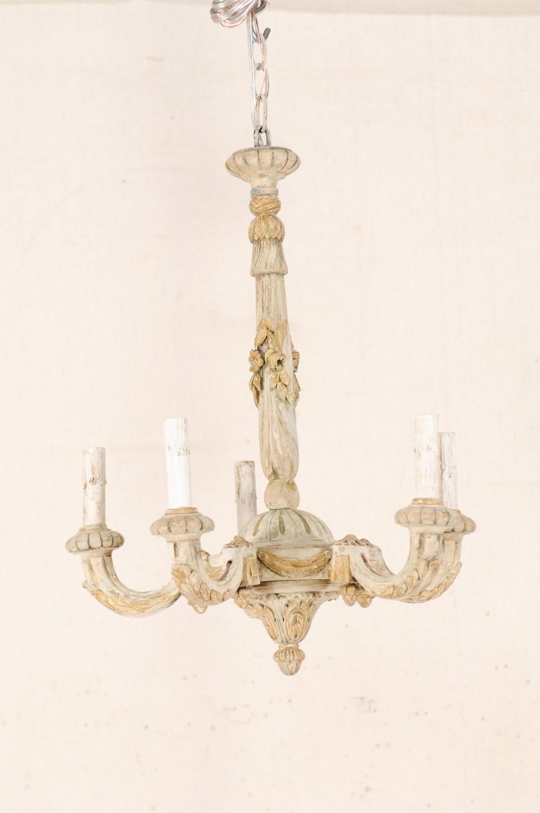 A cute French five-light painted and floral carved wood chandelier from the mid-20th century. This vintage chandelier from France features a central wood column, with tassel carved top, floral accents with ribbons wrapping down the mid-section, and