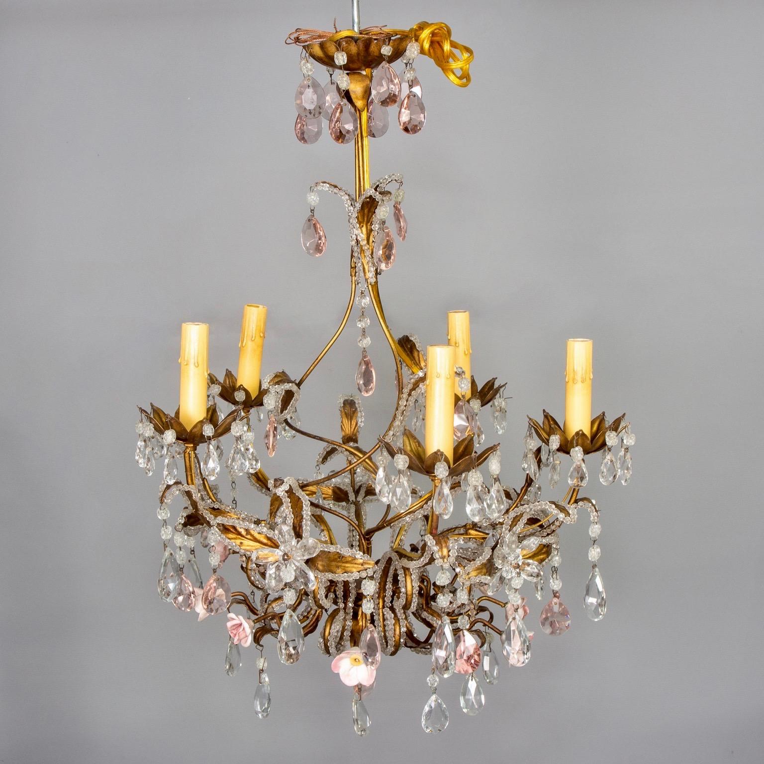 Five-light French gilt metal chandelier is embellished with clear and pink crystal drops, clear crystal flowers, extensive crystal beading and pale pink porcelain roses, circa 1930s. New wiring for US electrical standards. Candelabra sized sockets.