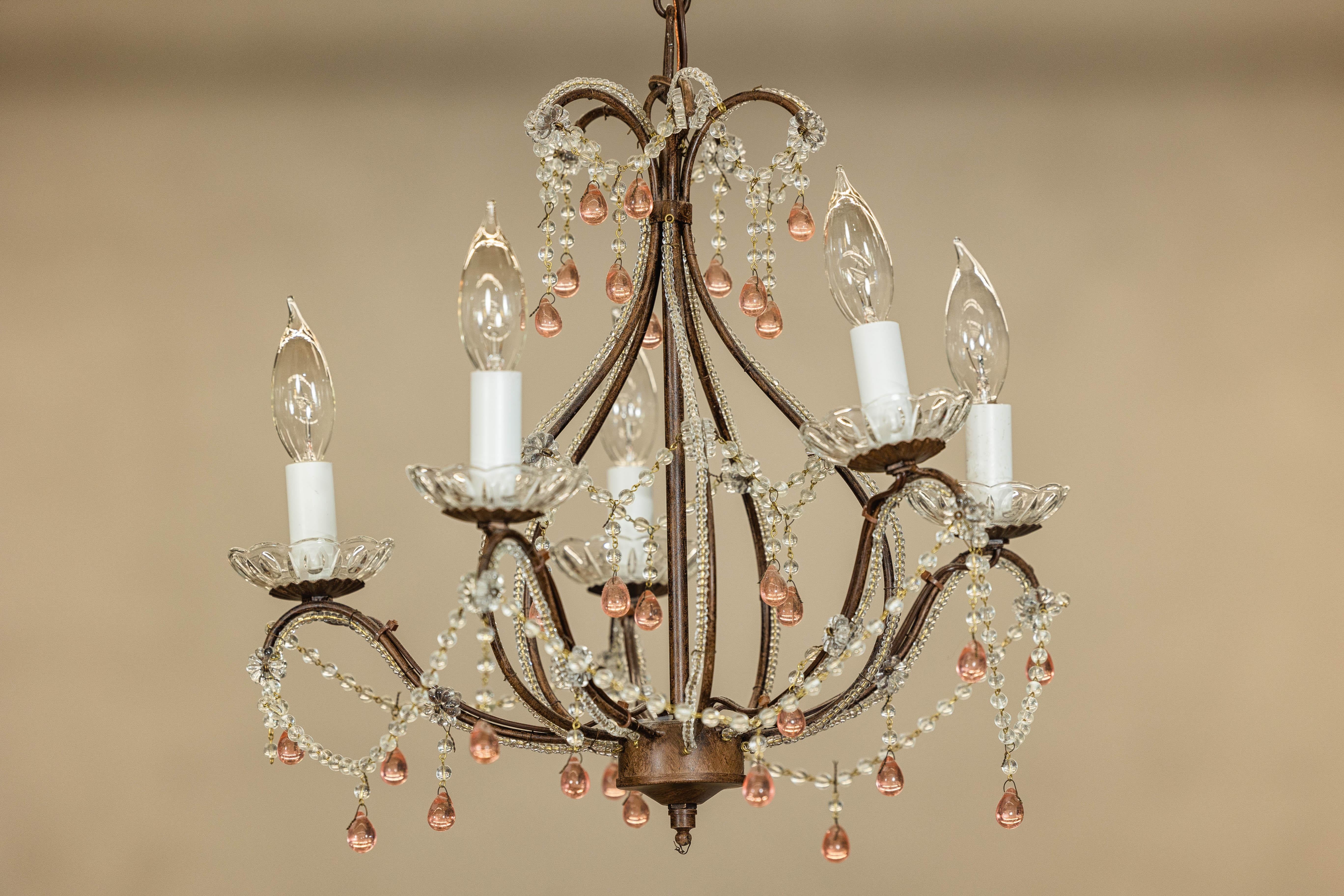 A French five-light crystal chandelier with pink glass teardrop pendants. Delicately crafted in France circa 1950, this vintage five-light crystal chandelier combines graceful curves with romantic charm. A hand-wrought iron frame, finished in a