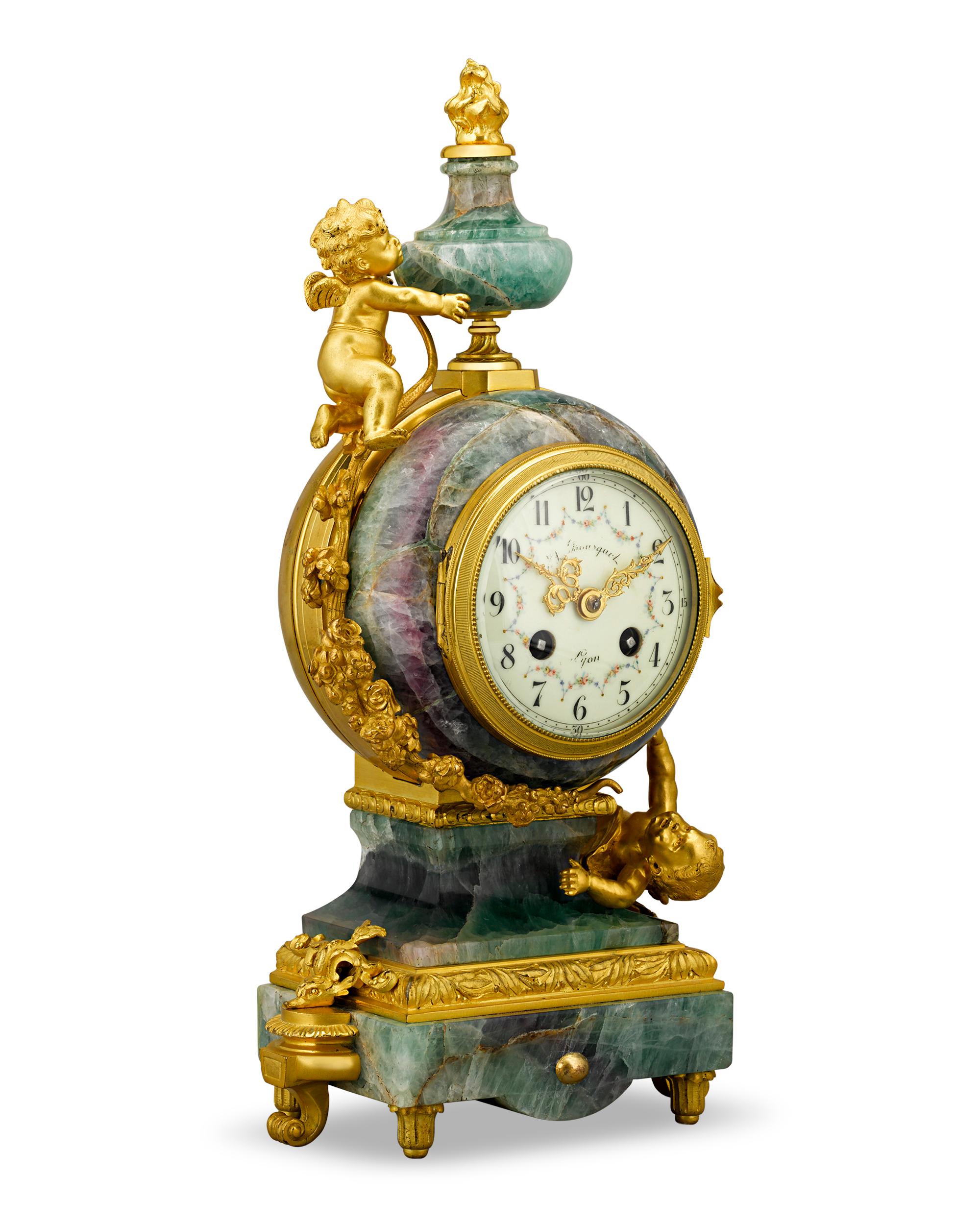 This beautiful French clock garniture, styled in the Louis XV taste, is a charming work of artistry and craftsmanship. Crafted of richly veined and brightly-hued fluorspar mounted with ornately cast ormolu bronze, this garniture celebrates classical