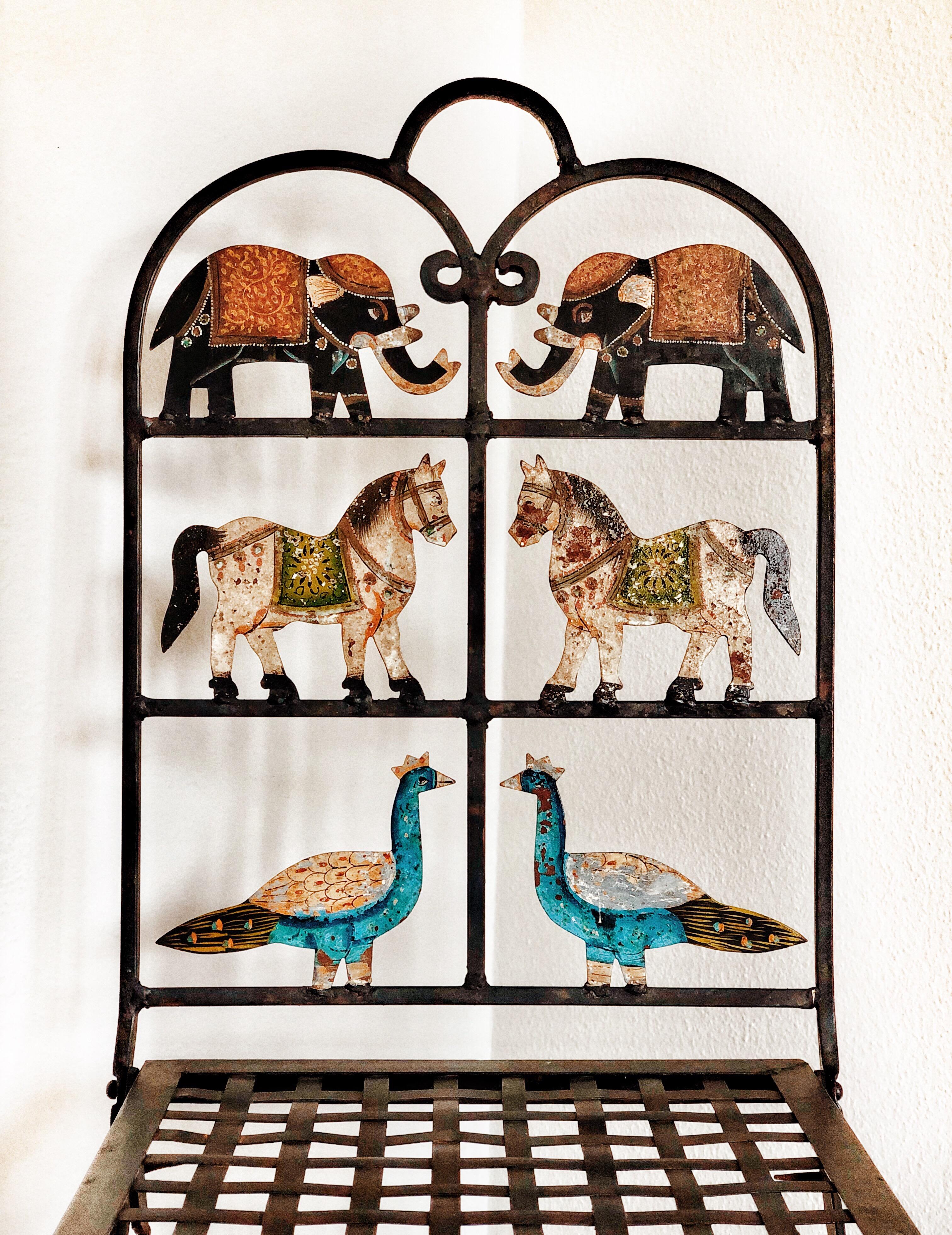 A whimsical pair of wrought iron folding garden chairs with painted animal cutouts, including elephants, horses and peacocks. These chairs are utterly charming, the weathering of the surface only adding to their appeal. They do fold and are suitable