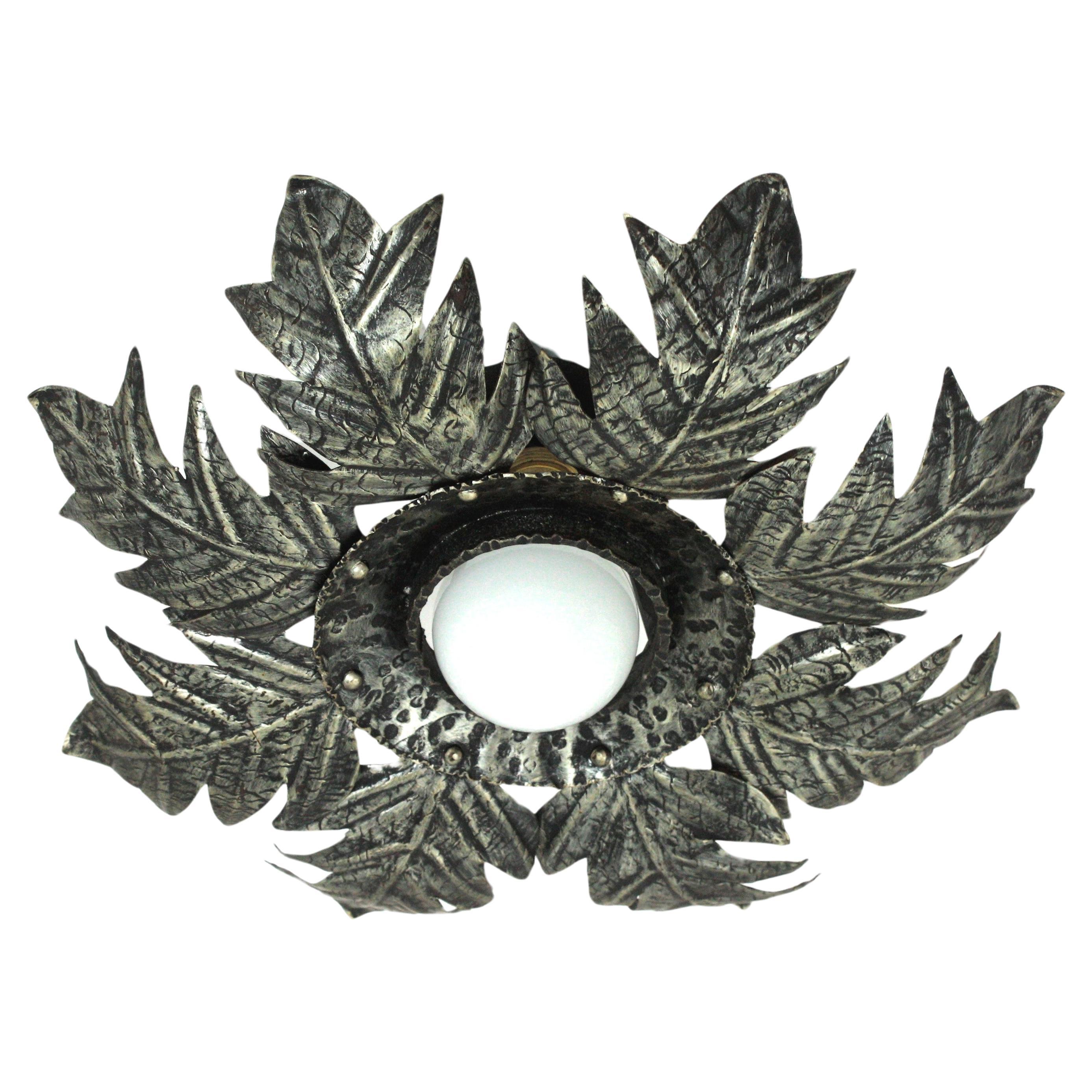 Eye-catching french sunburst leaves flush mount in silvered metal, 1950s.
This leafed sunburst ceiling light fixture has a beautiful construction with large leaves surrounding a central hand-hammered ring with nail accents.
It has a central light,