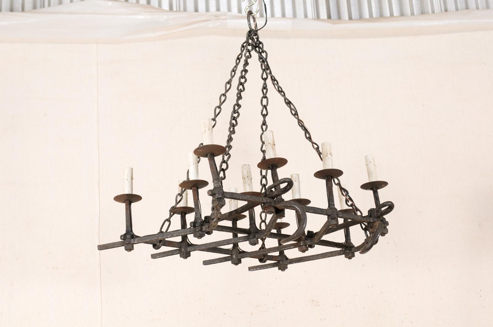 A French twelve-light forged iron chandelier from the mid-20th century. This vintage chandelier from France, which looks to have originally been an old farm implement that was retrofitted into a light fixture, has an overall rectangular-shape, with